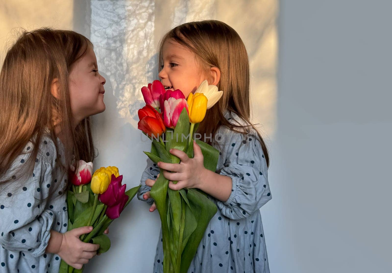 Portrait of two smiling little girl with a bouquet of tulips. Lifestyle, Women's or Mother's Day. Siblings or twin day. Space for text