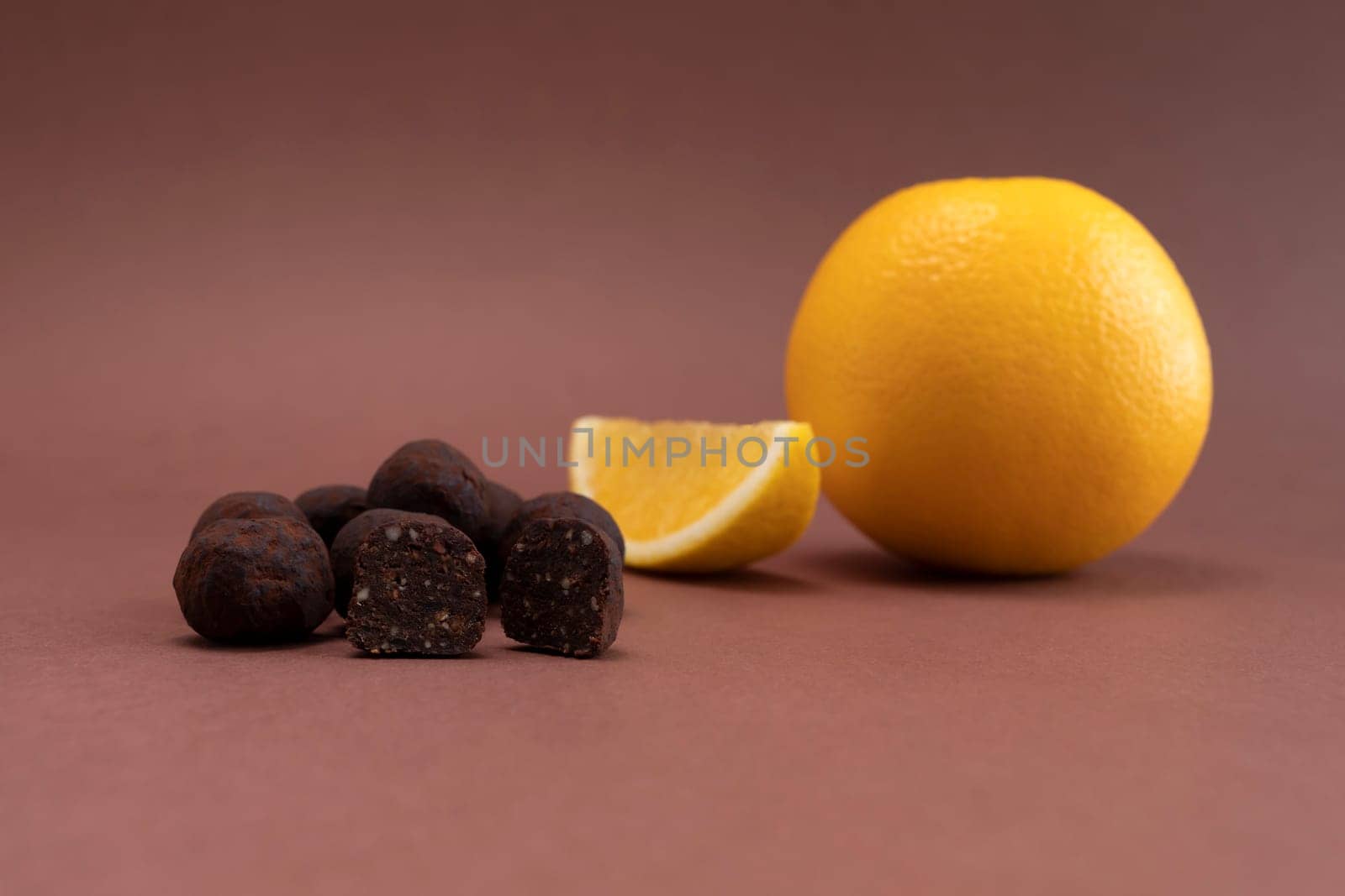 Vegan Raw Sweet Balls made of Organic Cocoa beans with Dry Citrus Fruits on Brown Background. Orange is beside. Horizontal Plane. Healthy Food, Dessert. High quality photo