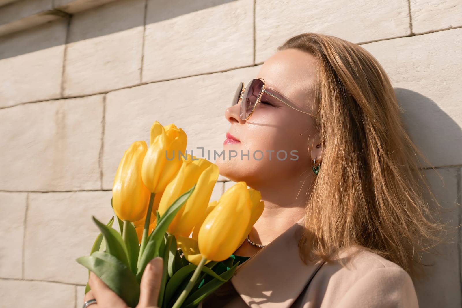 Woman holding yellow tulips, leaning against stone wall. Women's holiday concept, giving flowers