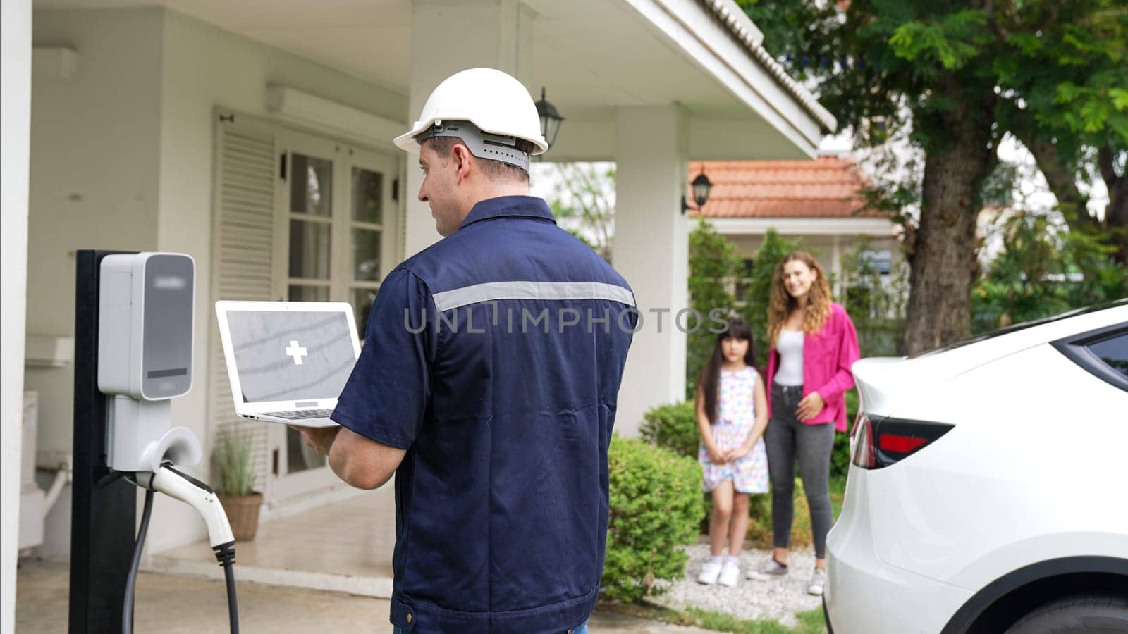 Qualified technician working on home EV charging station installation, making troubleshooting and configuration setup on charging system with empty laptop screem for EV at home. Synchronos