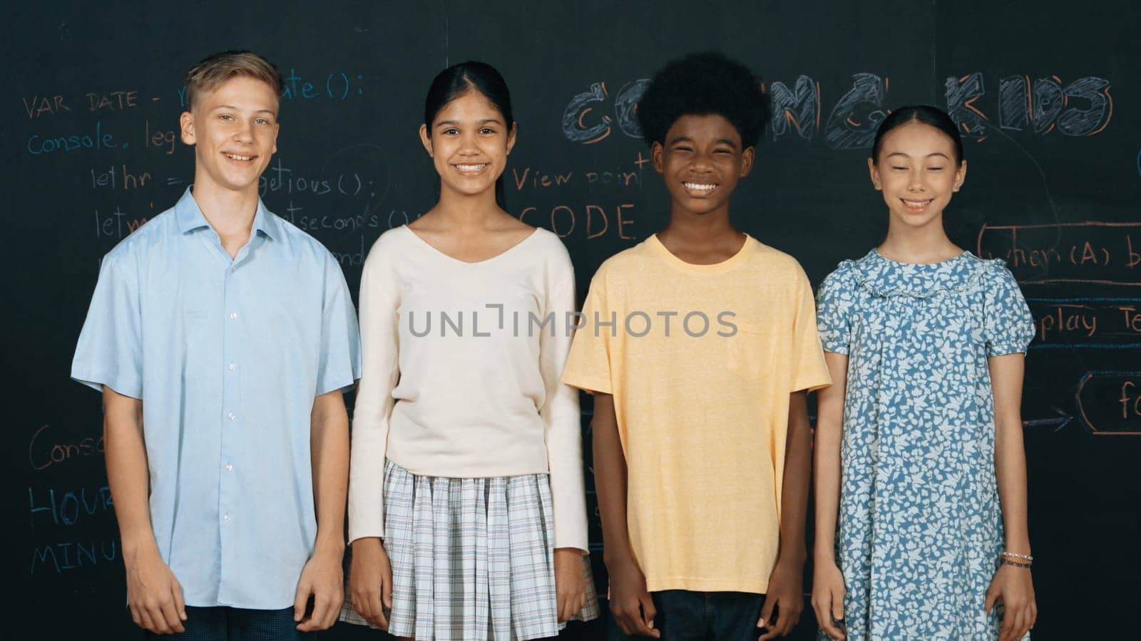 Group of smart multicultural teenager looking at camera at blackboard. Happy diverse children standing in STEM technology class with engineering code, prompt or planning program idea. Edification.