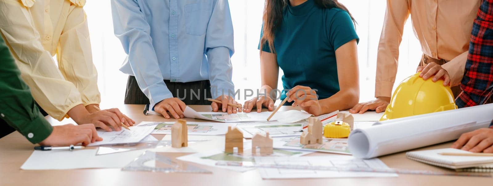 Professional architect engineer team discussion about architectural project on meeting table with wooden block and blueprint scatter around. Design and cooperate concept. Closeup. Delineation.