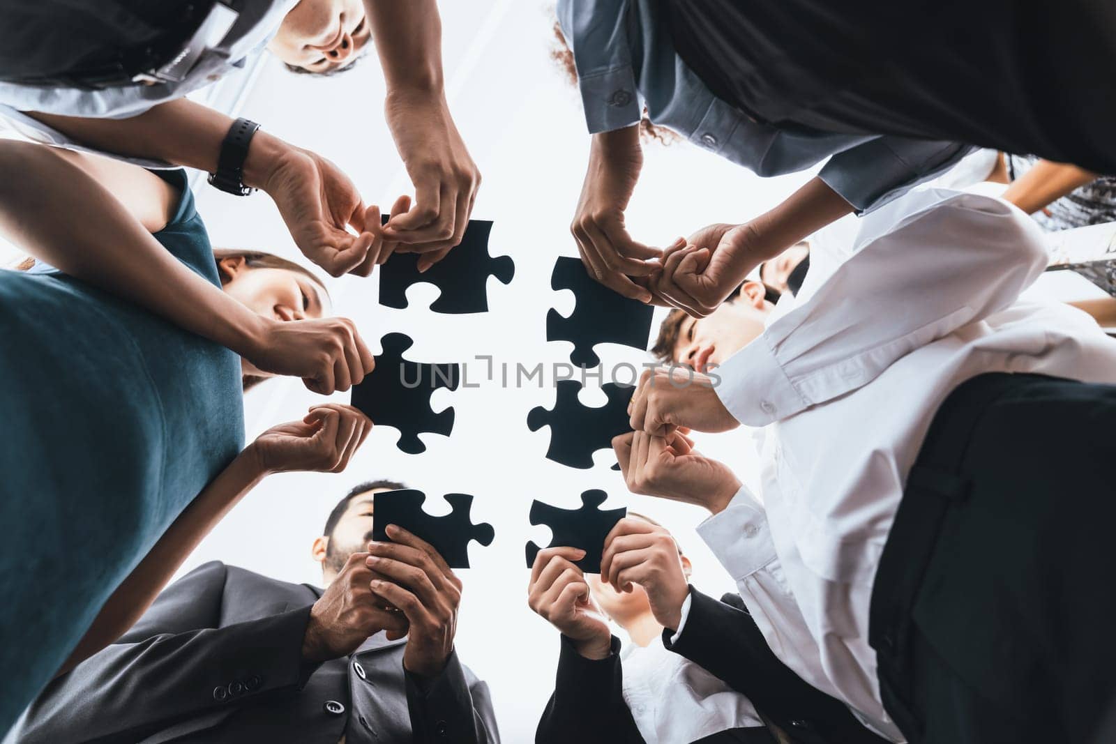 Below view of diverse corporate officer workers collaborate in office connecting puzzle pieces as partnership and teamwork concept. Unity and synergy in business idea by merging jigsaw puzzle. Concord