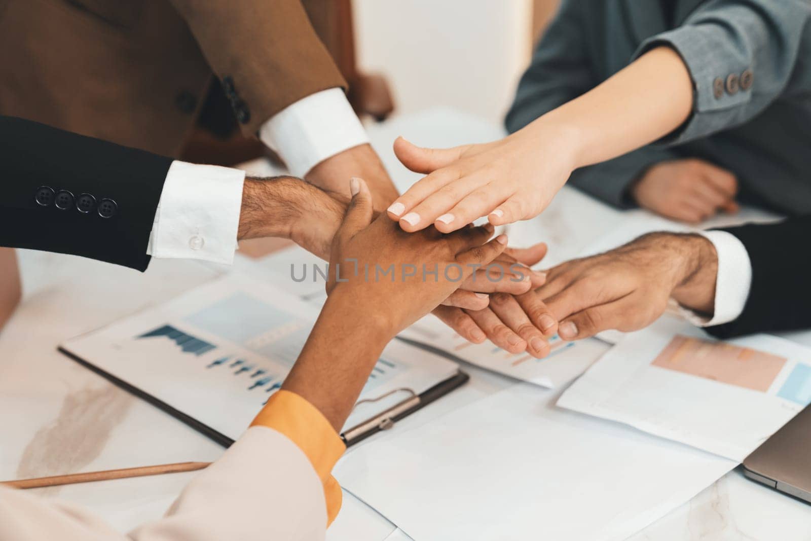 Top view of corporate diverse businesspeople putting hands together on meeting table with document scatter around at business meeting room. Represented unity, cooperation, collaboration. Ornamented.