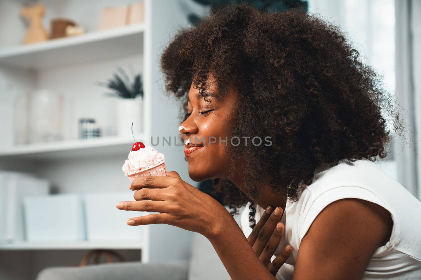 Funny African on mess face with whipped cream presenting cupcake topping on cherry in concept special pastel color. Content creating of social media with favorite sweets bakery dish. Tastemaker.