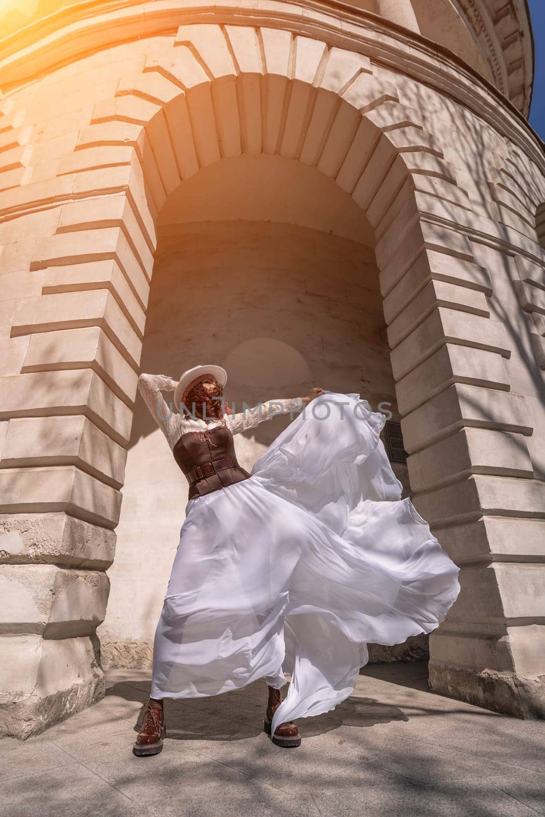 Stylish woman building city. A dancer in a long white skirt dances in front of a building with an arch. The skirt develops in the wind