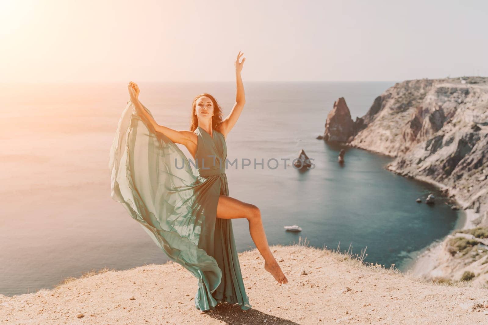 Woman green dress sea. Female dancer posing on a rocky outcrop high above the sea. Girl on the nature on blue sky background. Fashion photo