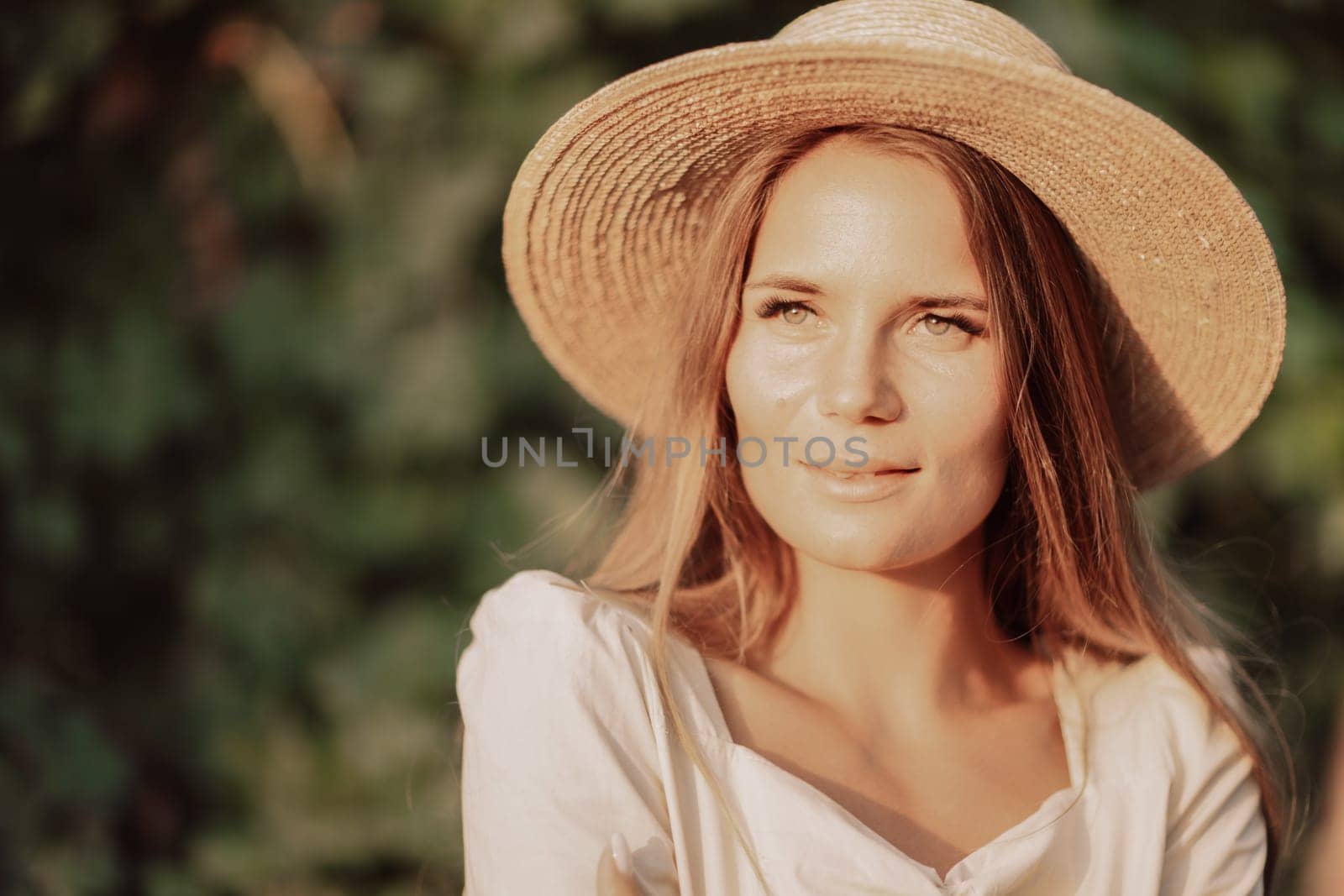 Woman with straw hat stands in front of vineyard. She is wearing a light dress and posing for a photo. Travel concept to different countries.