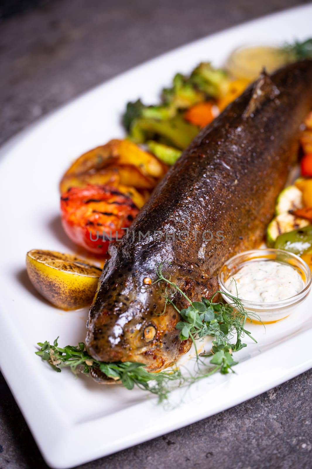 Trout fish with grilled vegetables on a white plate. Isolated on a black background. by Pukhovskiy