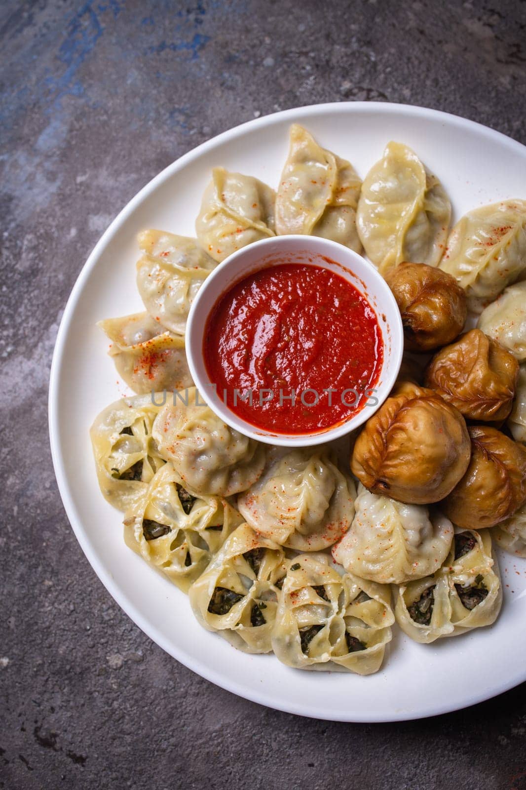 A delicious assortment of Uzbek dumplings with meat, pumpkin, and greens served on a plate with a side of red sauce