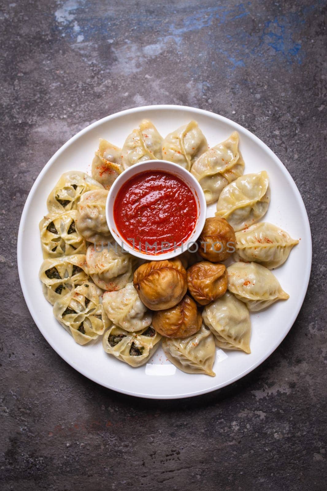 Uzbek samsas and manti with meat, pumpkin and greens on a plate with red sauce by Pukhovskiy