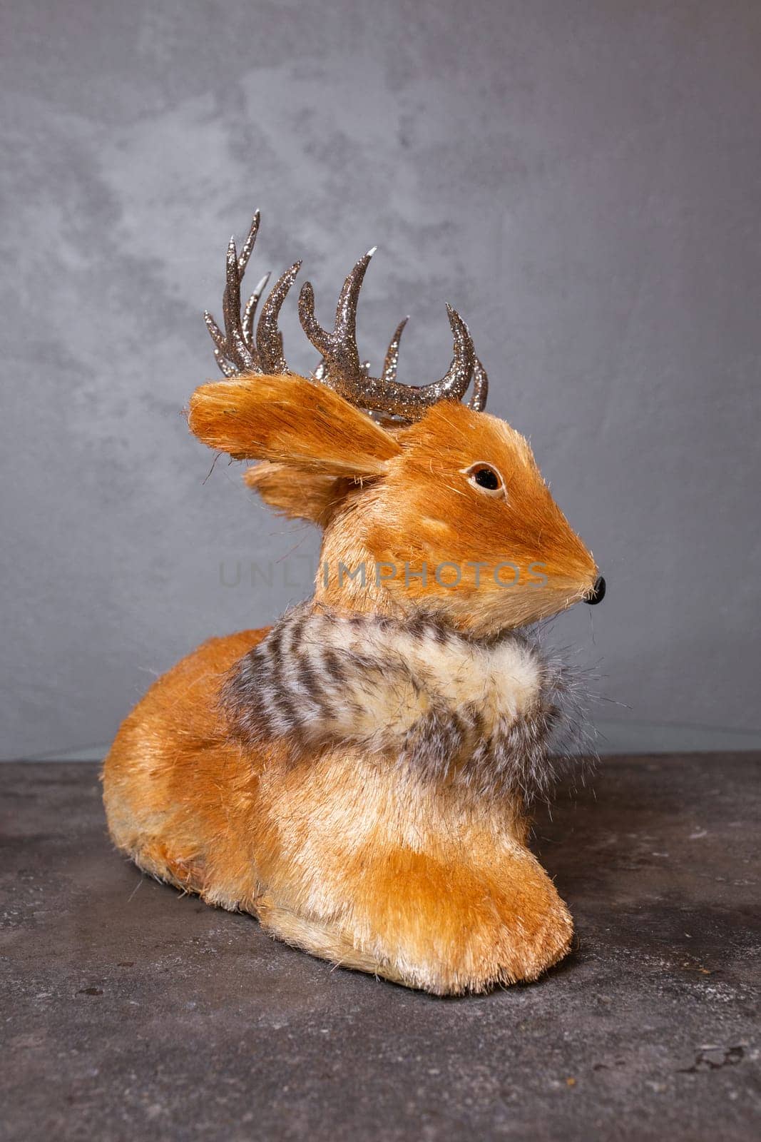 Small brown deer figurine with silver antlers and black nose and hooves, placed on a gray surface and facing the camera.