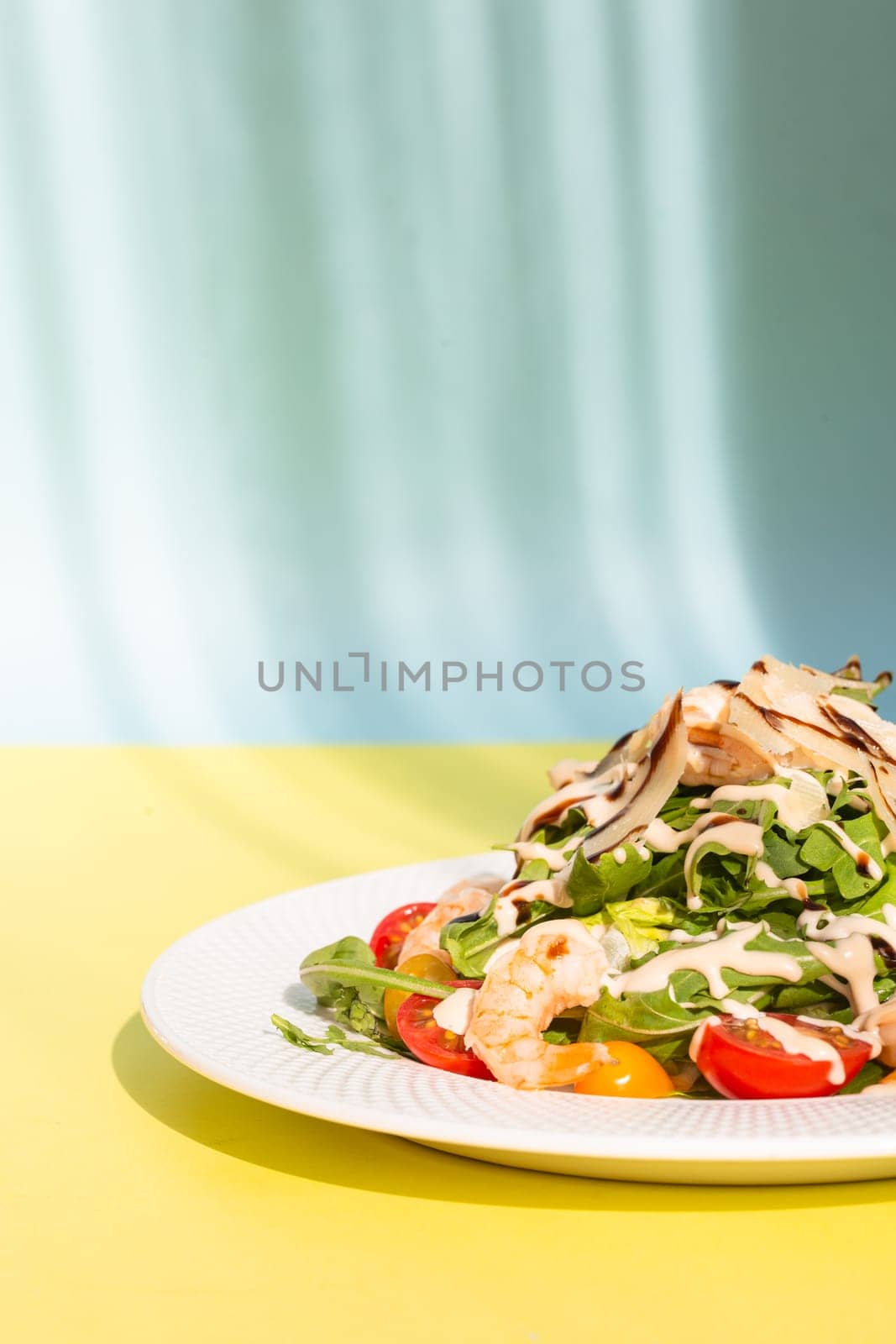 Fresh salad with greens, tomatoes, grilled shrimps on white plate. On yellow background. by Pukhovskiy