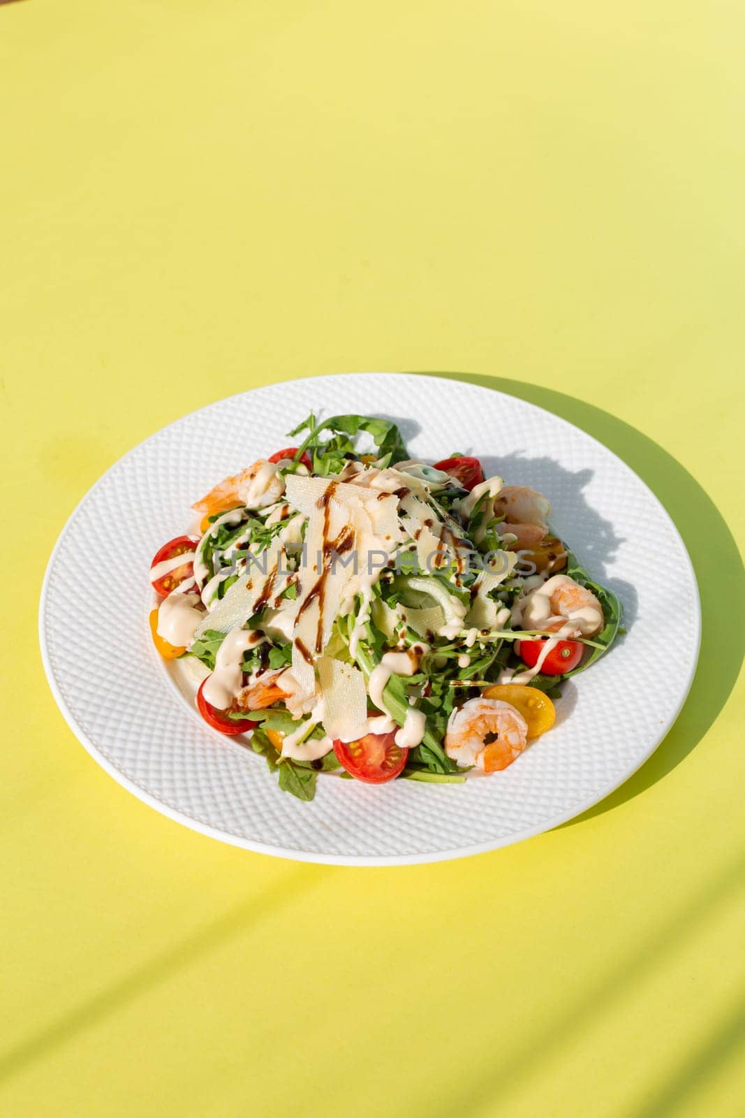 Fresh salad with greens, tomatoes, grilled shrimps on white plate. Top view on yellow background. by Pukhovskiy