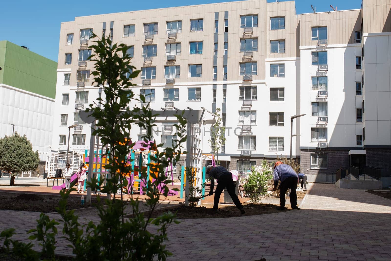 Modern apartment buildings with a courtyard playground. Contemporary design, large windows, balconies. Playground with swings, slide, climbing frame.