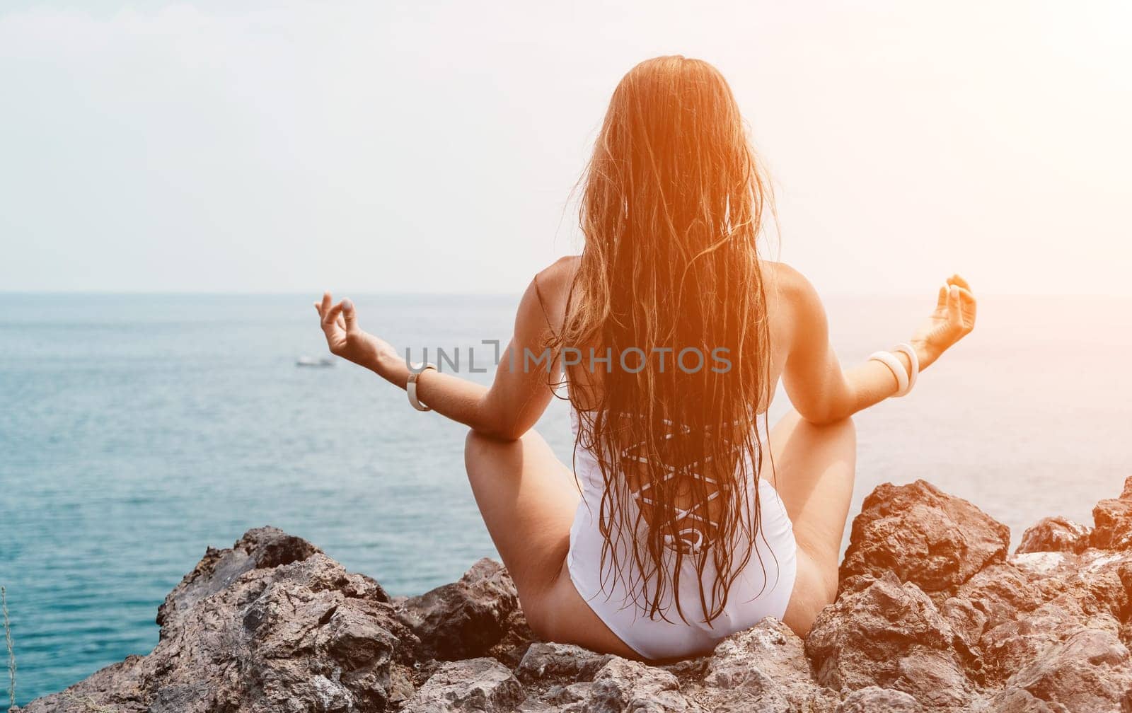 Woman meditating in yoga pose silhouette at the ocean, beach and rock mountains. Motivation and inspirational fit and exercising. Healthy lifestyle outdoors in nature, fitness concept.