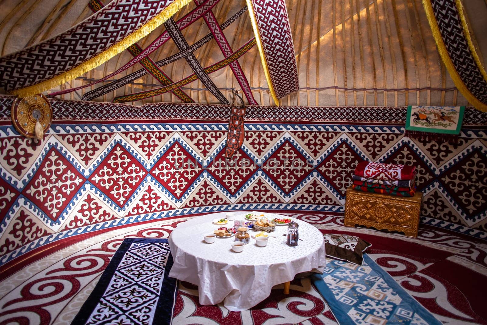 Interior of a kazak yurt with felt carpets, furniture, and a table. Traditional nomadic dwelling with white tablecloth.