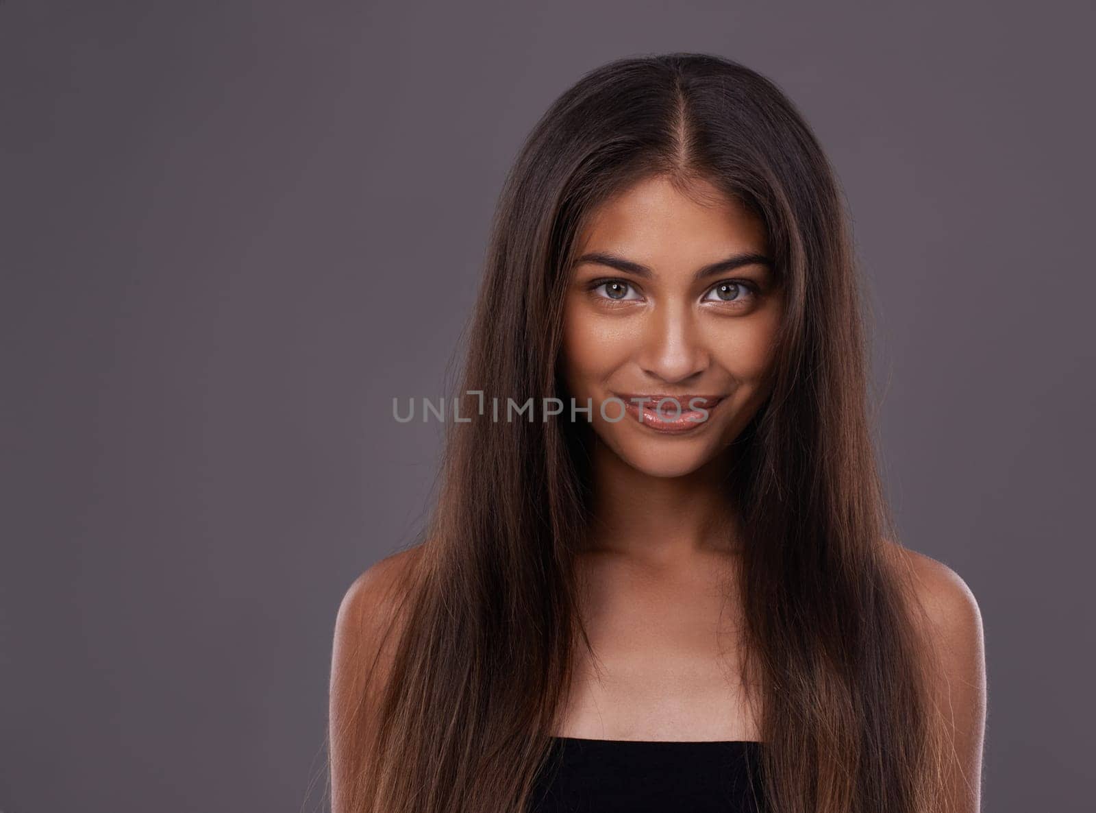 Portrait, hair care and Indian woman with cosmetics, treatment and grooming routine on a grey studio background. Face, person and model with volume or texture with keratin and healthy shine with glow.