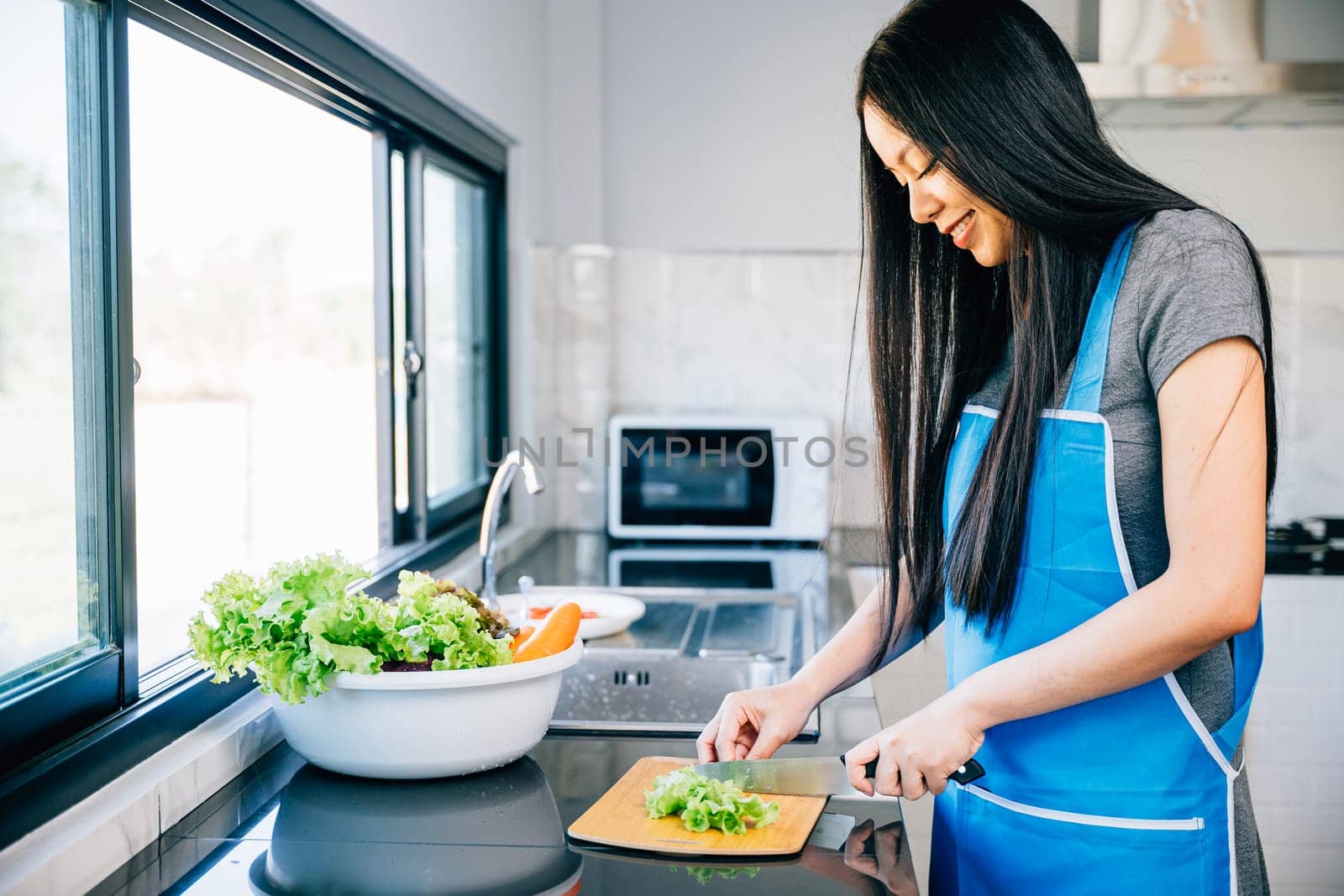 Close-up of a smiling woman in an apron cutting vegetables for a healthy salad. Emphasizing the housewife's preparation of a nutritious family meal in the kitchen.