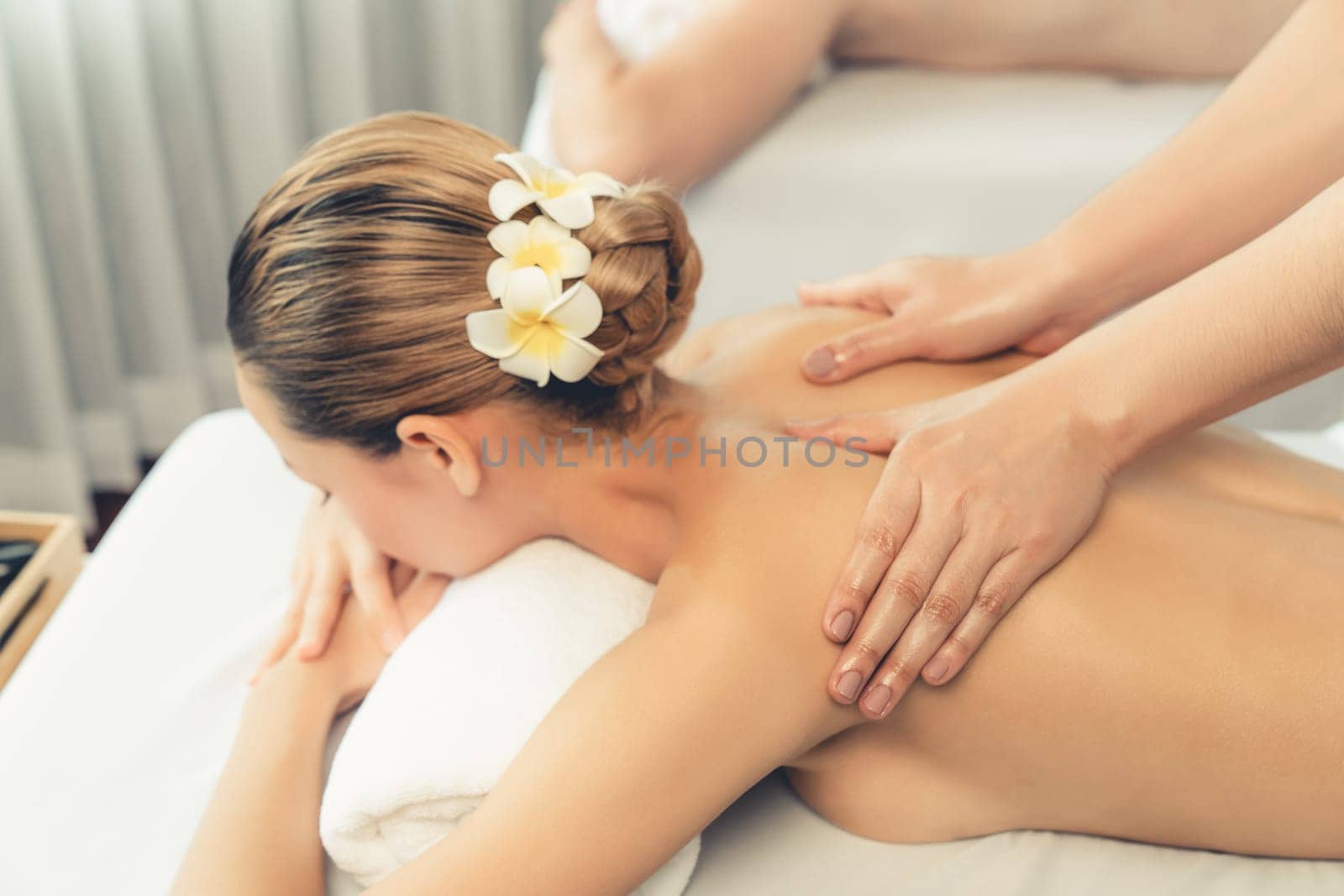 Caucasian couple customer enjoying relaxing anti-stress spa massage and pampering with beauty skin recreation leisure in day light ambient salon spa at luxury resort or hotel. Quiescent