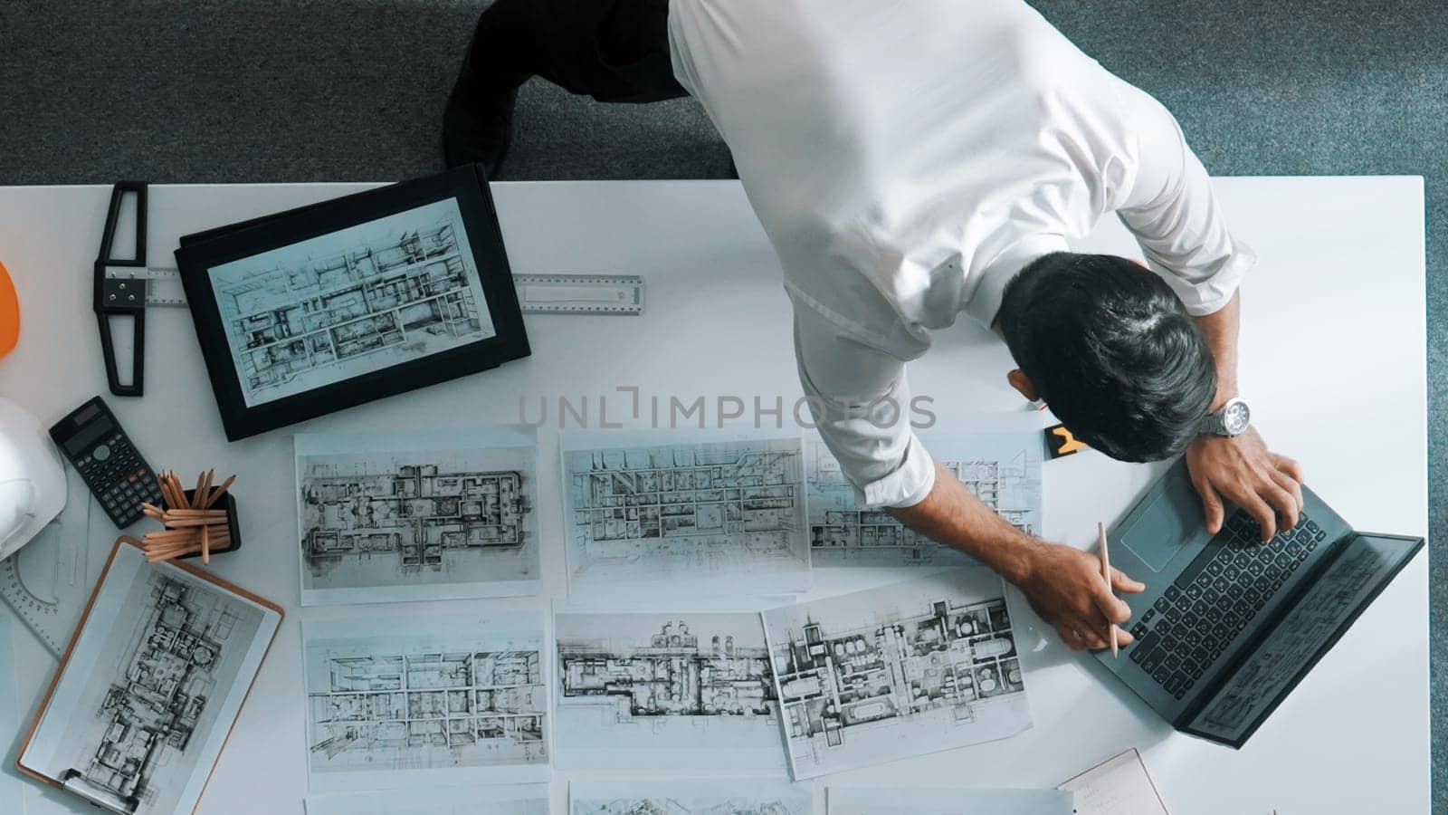 Top down view of engineer looking at tablet while using laptop to analysis building structure. Aerial view of architect checking at interior design at meeting table with project plan. Alimentation.