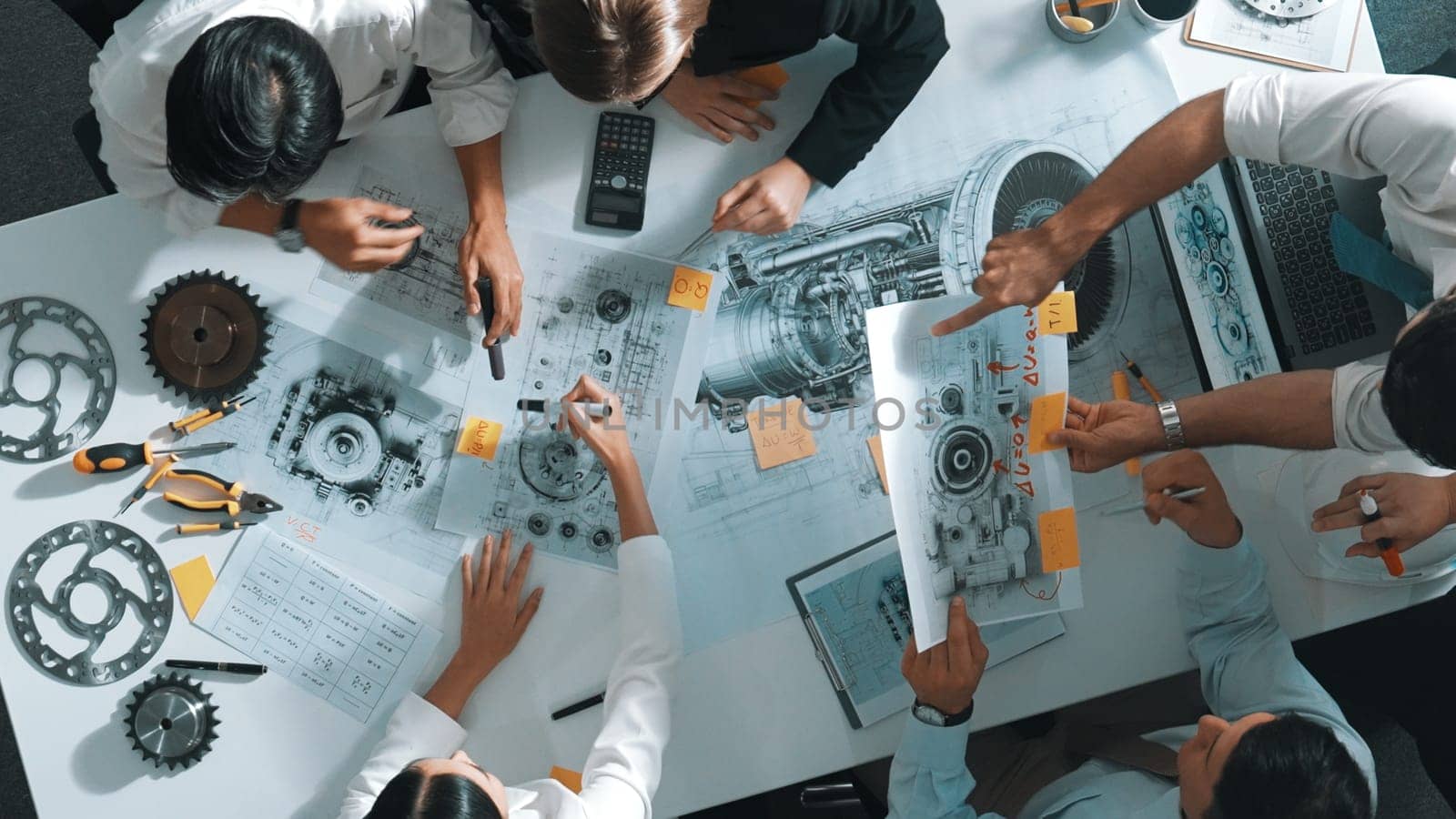 Top down aerial view of smart engineer team working together to design turbine engine. Professional technician discussing about jet engine construction while pointing at part of engine. Alimentation.