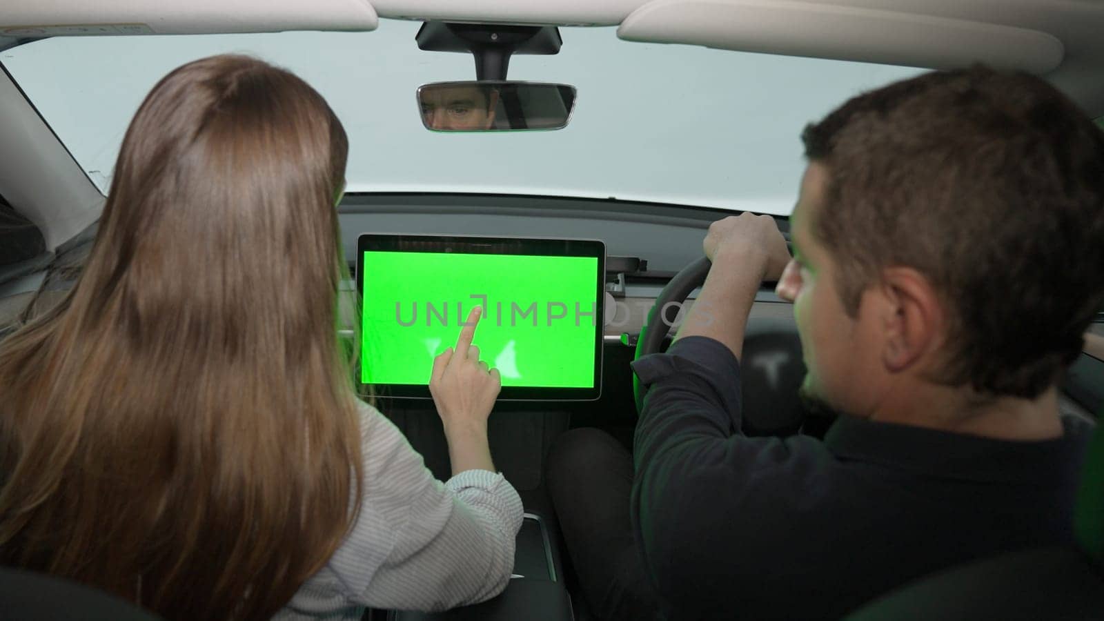 Holiday vacation road trip with environmental-friendly car concept. Eco-conscious young couple on driver seat holding blank copyspace green screen car's monitor for EV battery status. Exalt