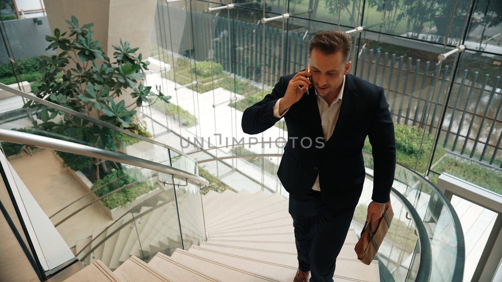 Smart businessman walking up spiral stair case and calling manager by using smart phone. Top view of manager talking marketing team by using telephone while going up stair at modern building. Urbane.