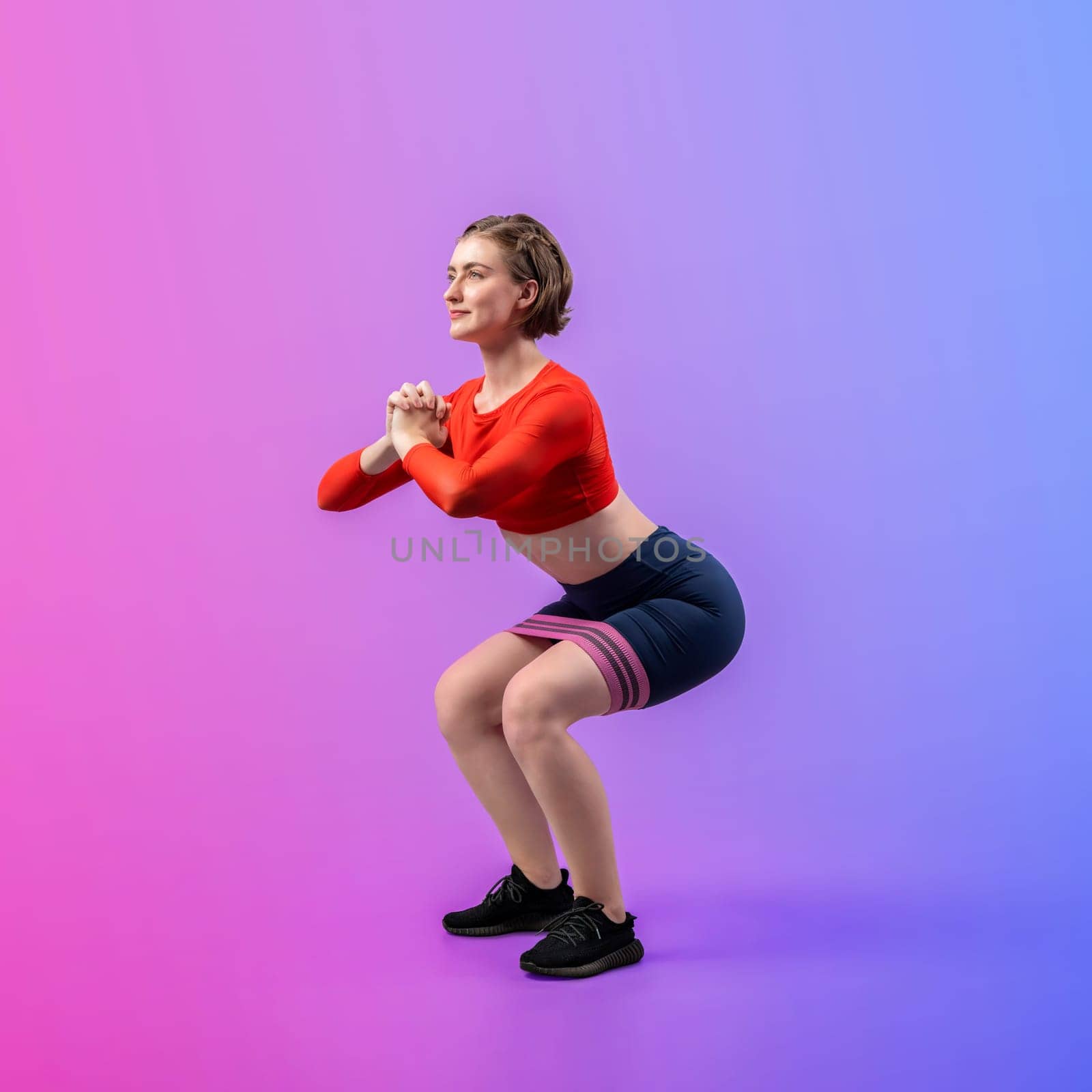 Full body length gaiety shot athletic and sporty young woman with fitness elastic resistance band in squat exercise posture on isolated background. Healthy active and body care lifestyle.