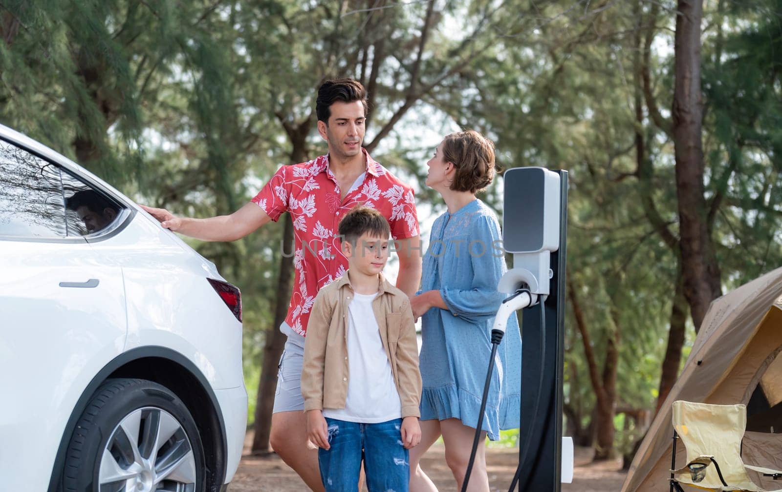 Outdoor adventure and family vacation camping in nature travel by eco friendly car for sustainable future. Lovely family recharge EV car with EV charging station in campsite. Perpetual