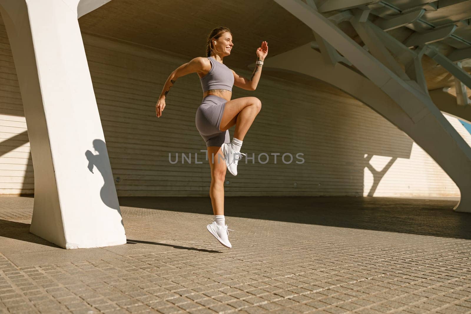 Young fit woman in sportswear leaping in the air with wall backdrop outdoors. High quality photo