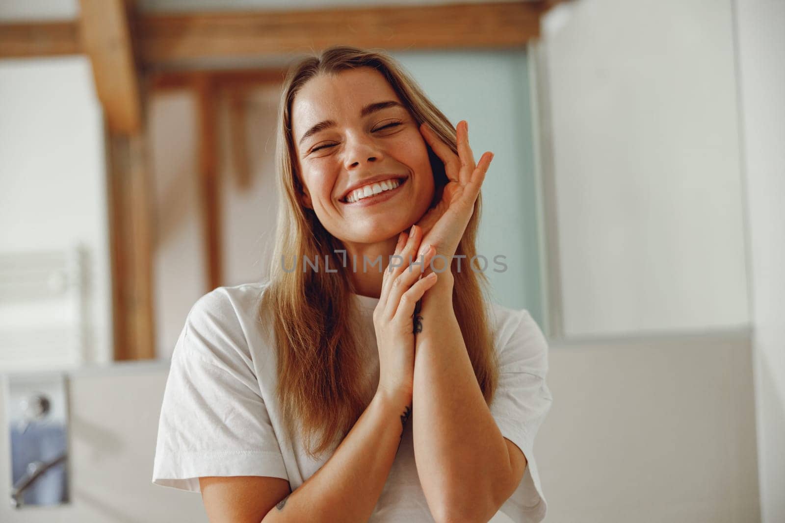 Attractive woman touching her pretty face and smiling while standing in bathroom by Yaroslav_astakhov