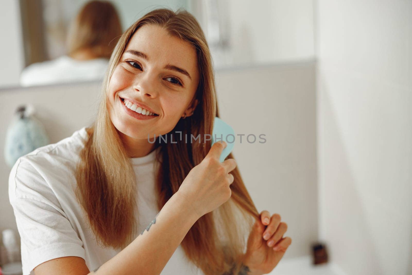 Woman standing at bathroom and combing her hair with brush after shower