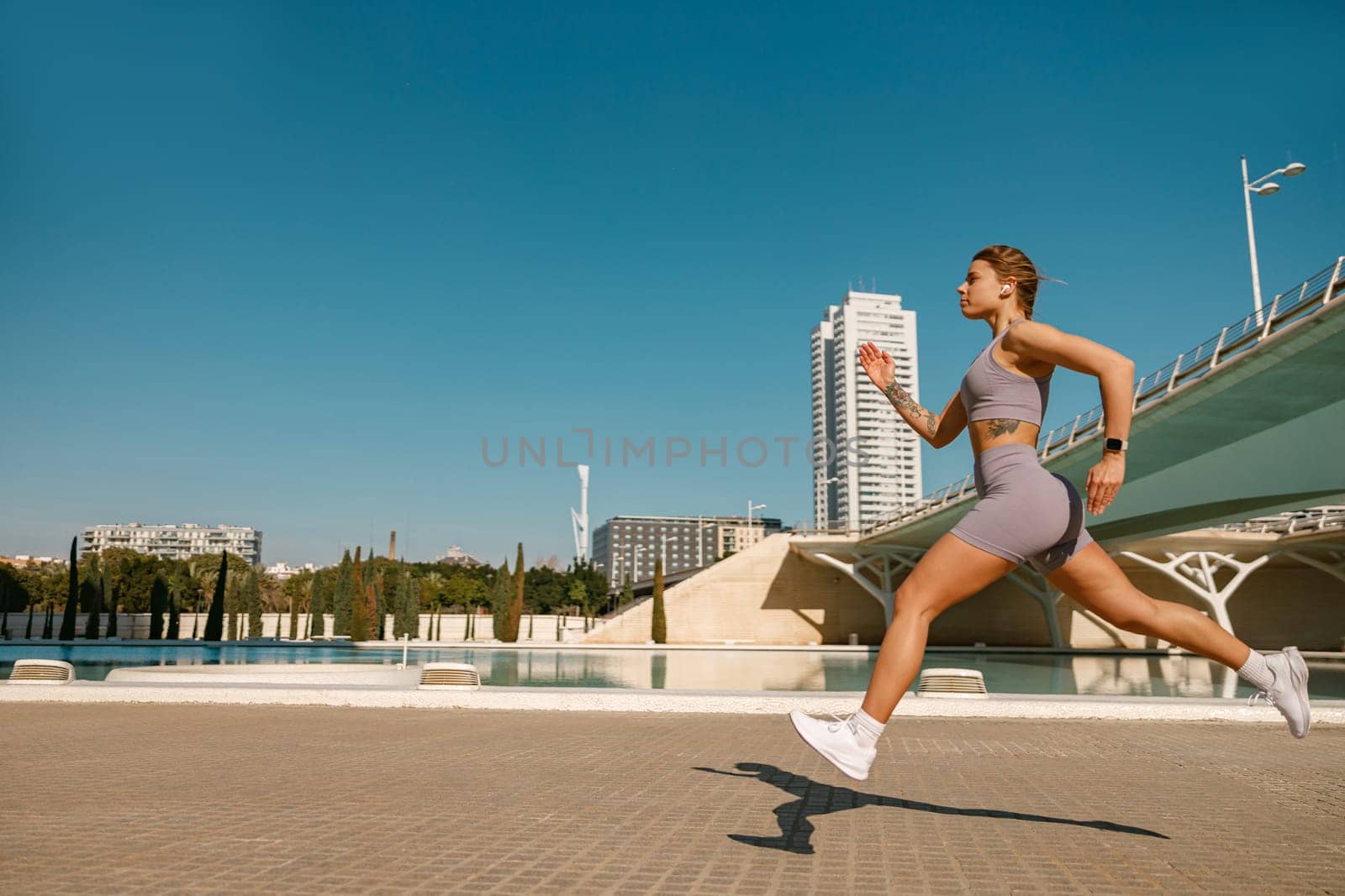 Young woman in sportswear is running on modern buildings background. Active lifestyle concept by Yaroslav_astakhov