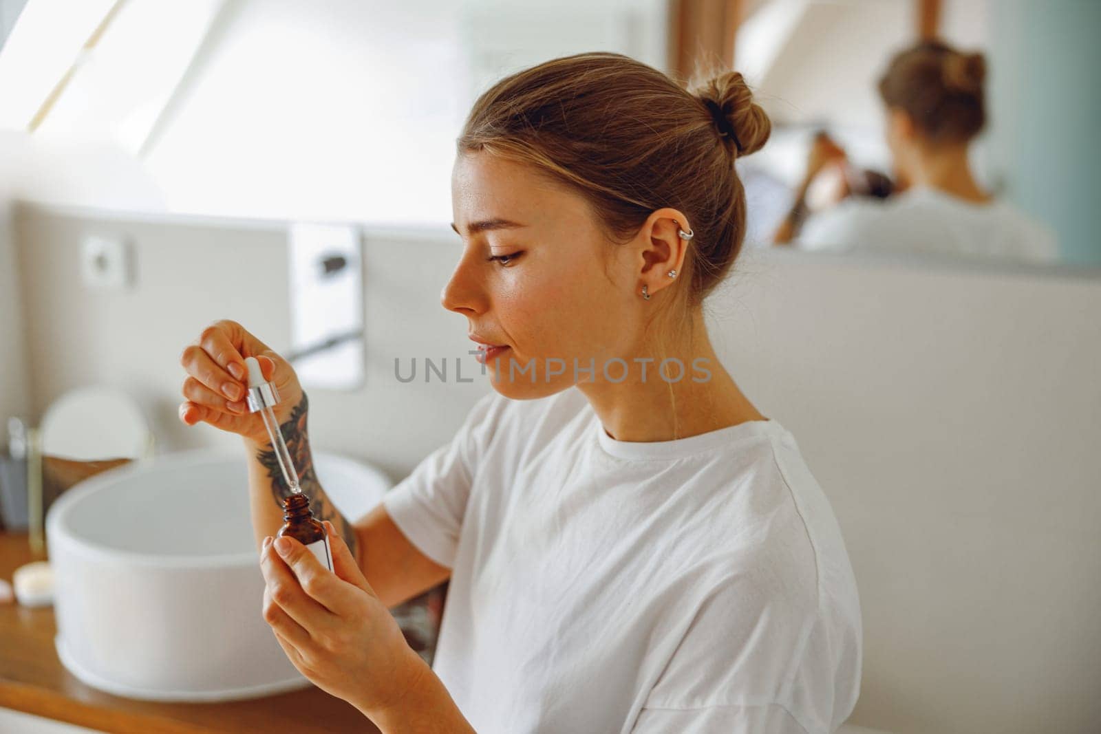 Attractive female applying serum on face moisturizing and caring for skin standing in bathroom