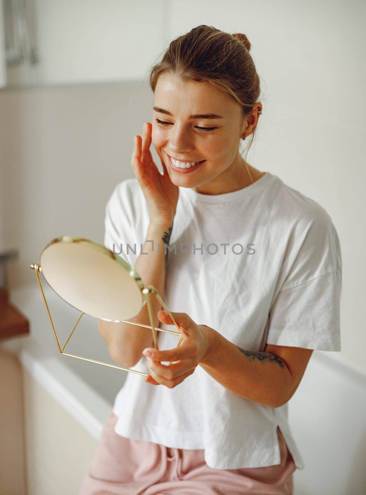 Smiling beautiful lady looking at her face in a small round mirror doing routine skincare procedures