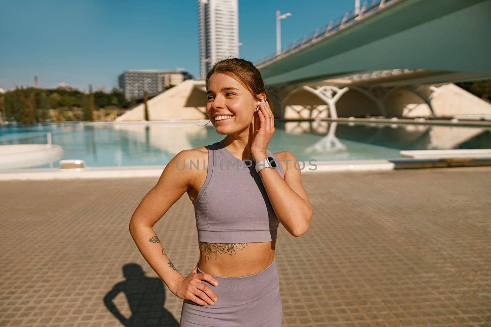 Smiling woman in sportswear have a rest after workout outside standing on building background by Yaroslav_astakhov
