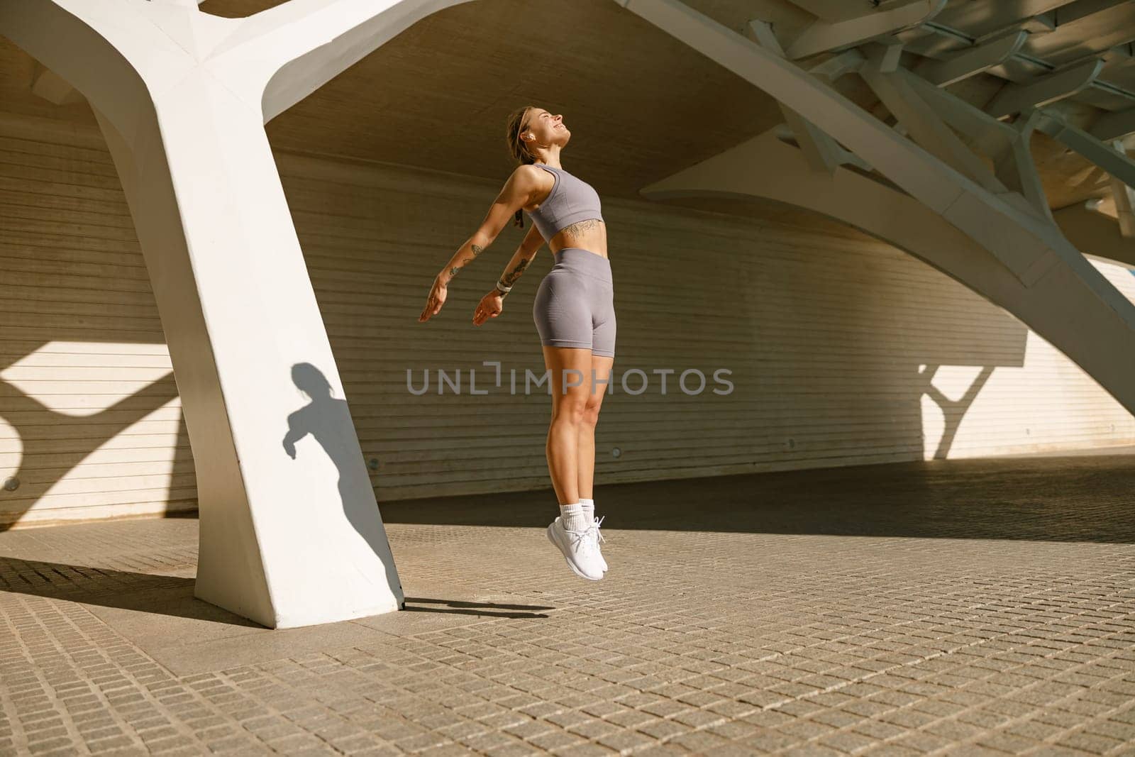 Young fit woman in sportswear leaping in the air with wall backdrop outdoors. High quality photo by Yaroslav_astakhov