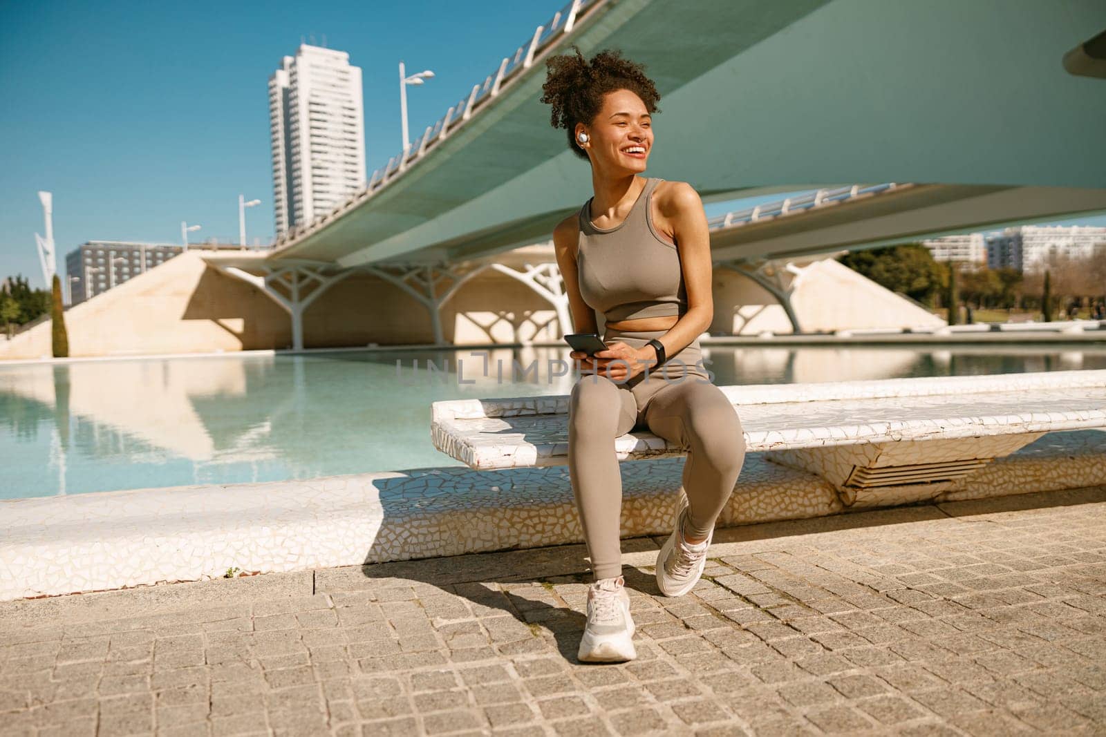 Fit woman in sportswear sitting outdoors after training and use mobile phone