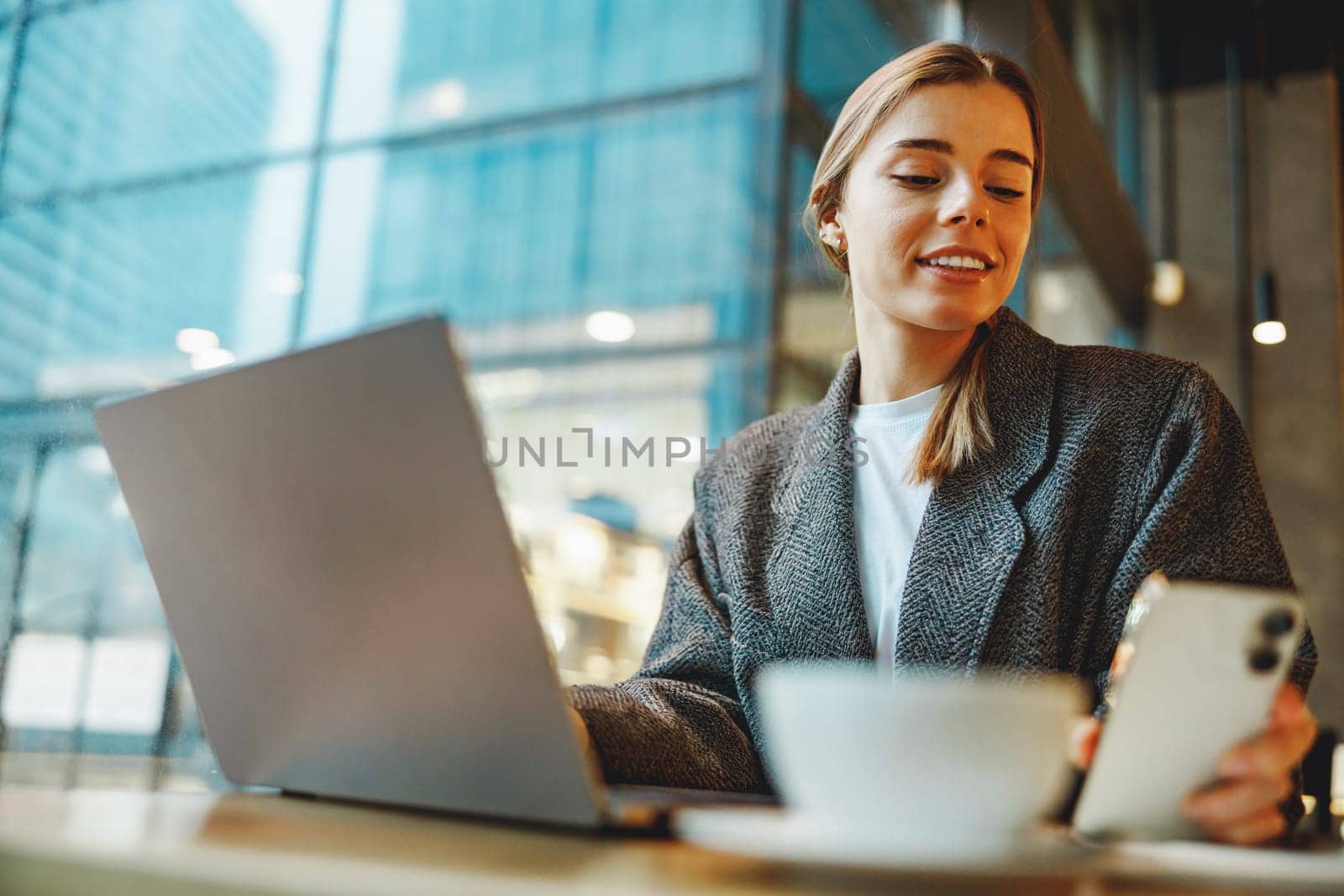 Smiling woman manager is using phone and work on laptop outside of office. Distance work concept