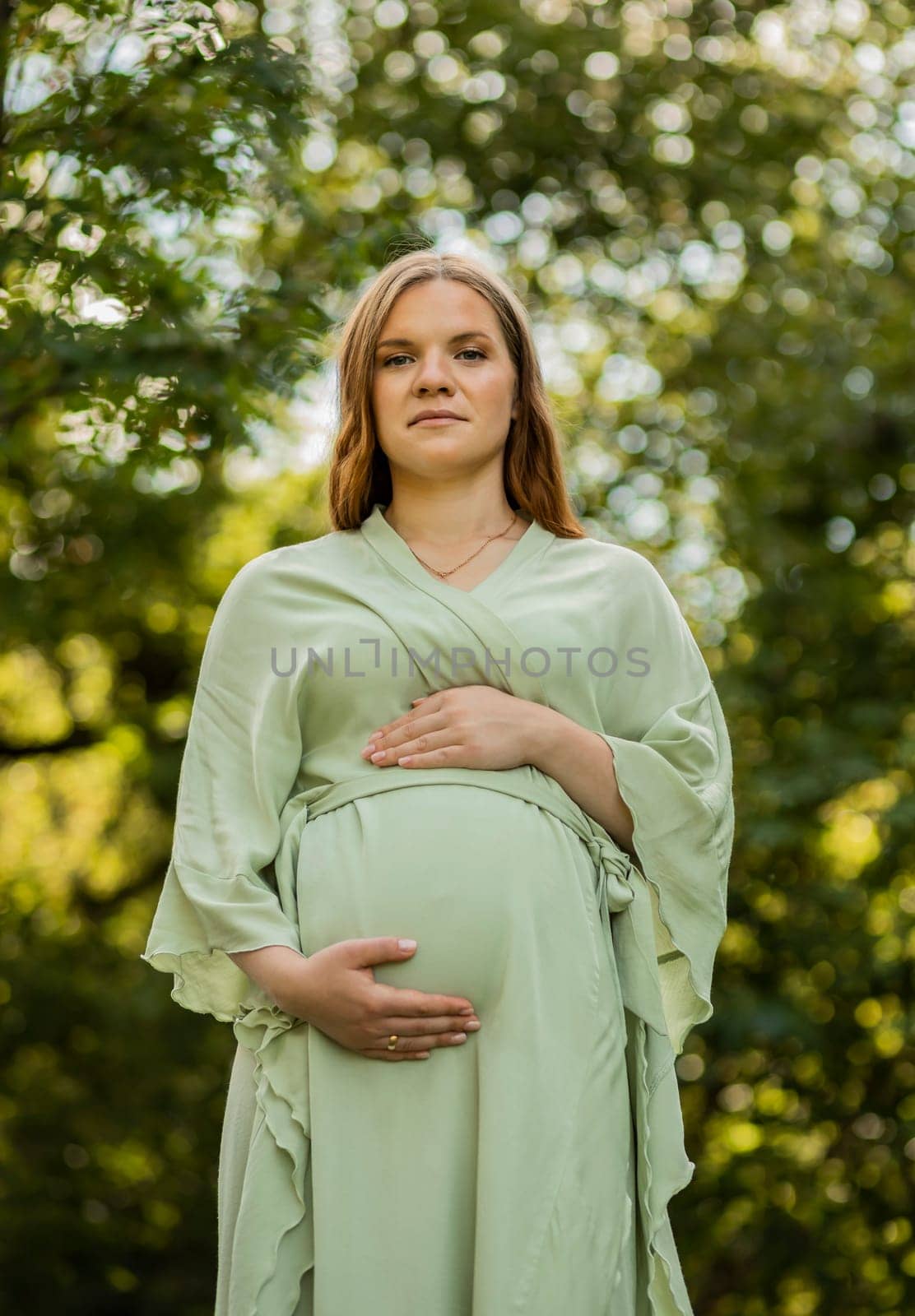 Young pregnant woman puts hands on big belly, green trees,blue sky on background. Female wears dress. Magic happy pregnancy. Child delivery preparation,emotional connection with baby.Vertical by netatsi
