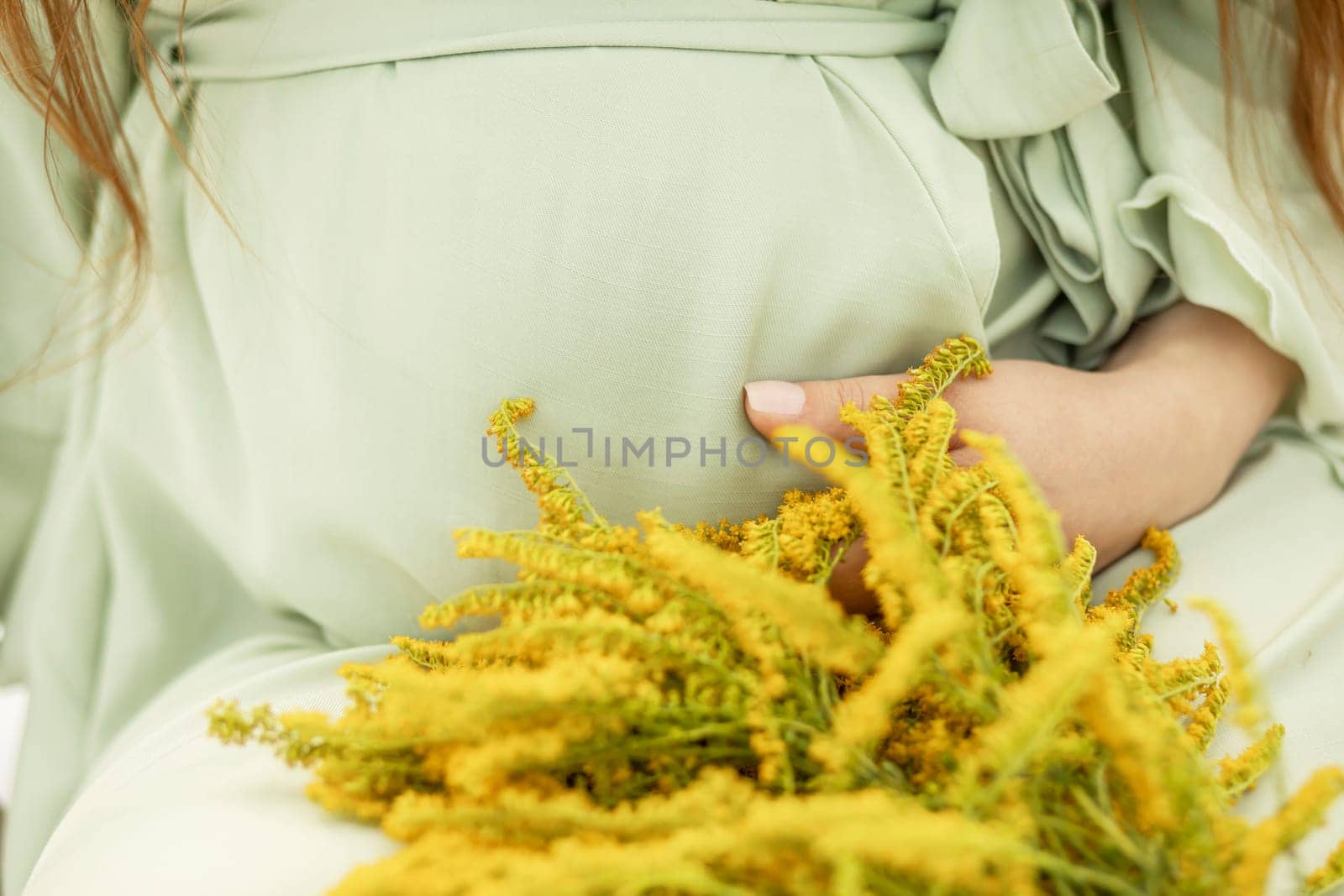 Cropped big belly of pregnant woman with yellow flowers Goldenrod.White female wears dress.Magic happy pregnancy. Childbirth preparations, emotional connection with baby. Baby shower. Horizontal by netatsi