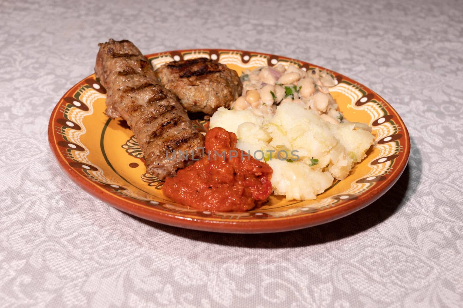 Plate With Traditional Bulgarian Food. Mashed Potato, Vegetable Relish Ljutenica, White Beans, Haricot, Grilled Minced Meat With Spices Kebapche. Horizontal Plane. High Quality Photo