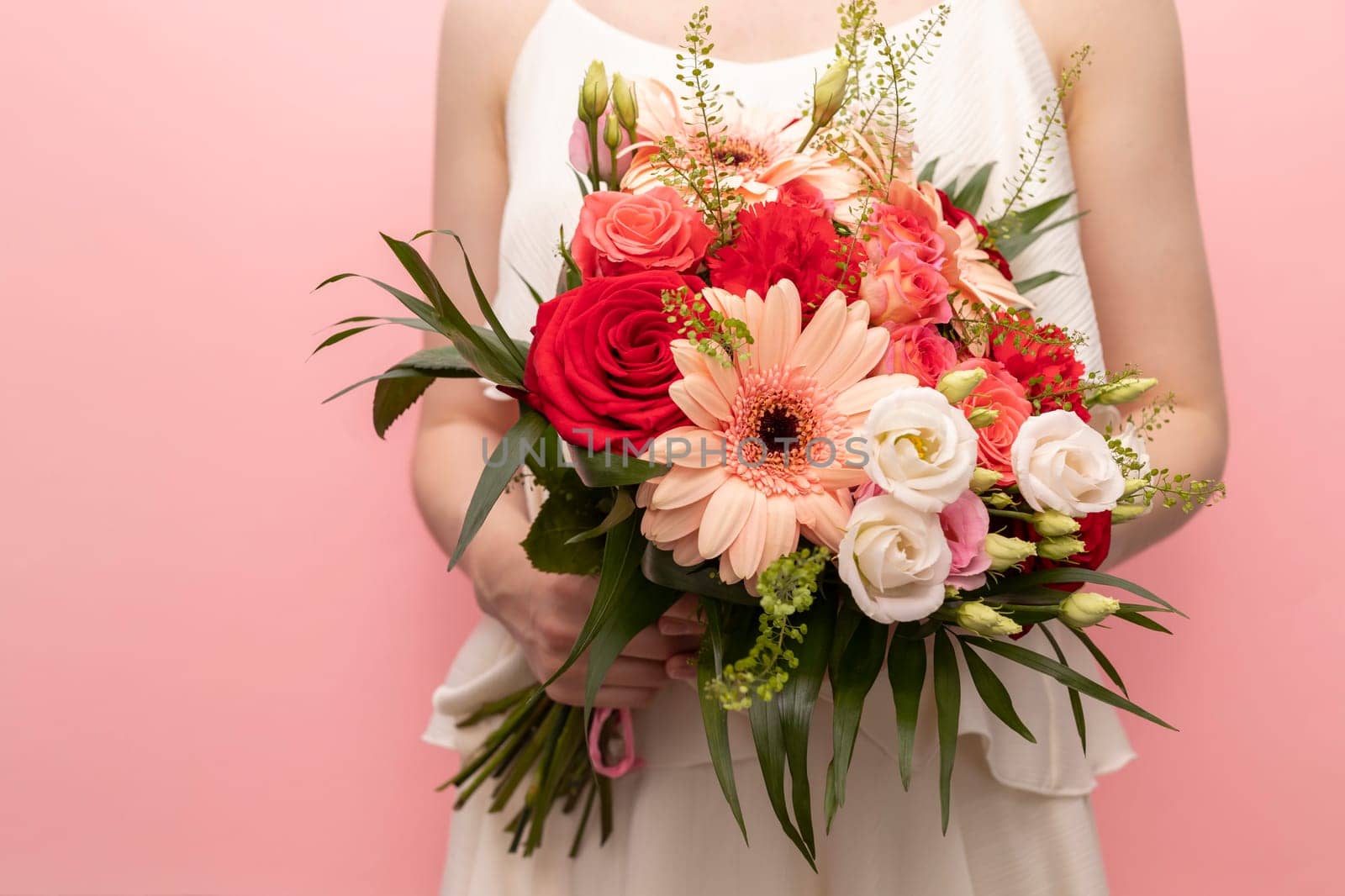 Cropped Woman Holds Beautiful Fresh Bouquet Of Flowers For Wedding Or Occasion On Pink Background. Colorful Mixed Roses, Carnation Shabot, Green Leaves, Gerber. Horizontal Plane by netatsi