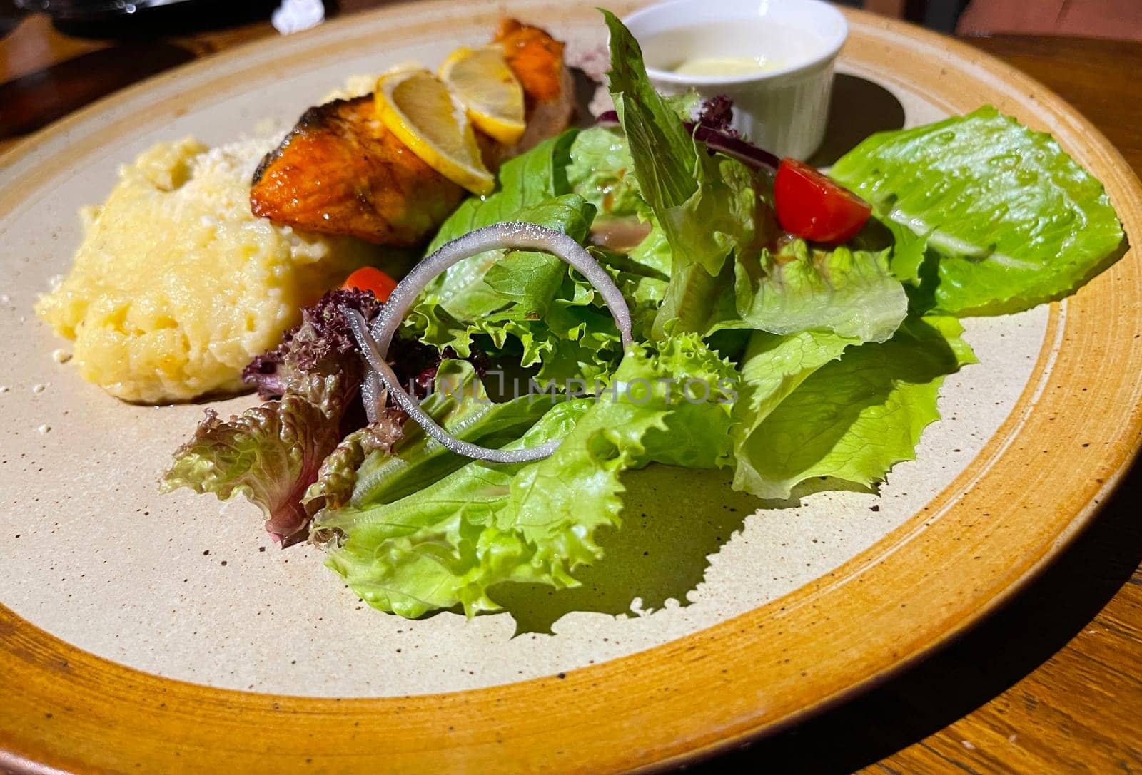 smoked grilled salmon fish served with salad and mash potatoes with lemons on top, served in plate perfect meal