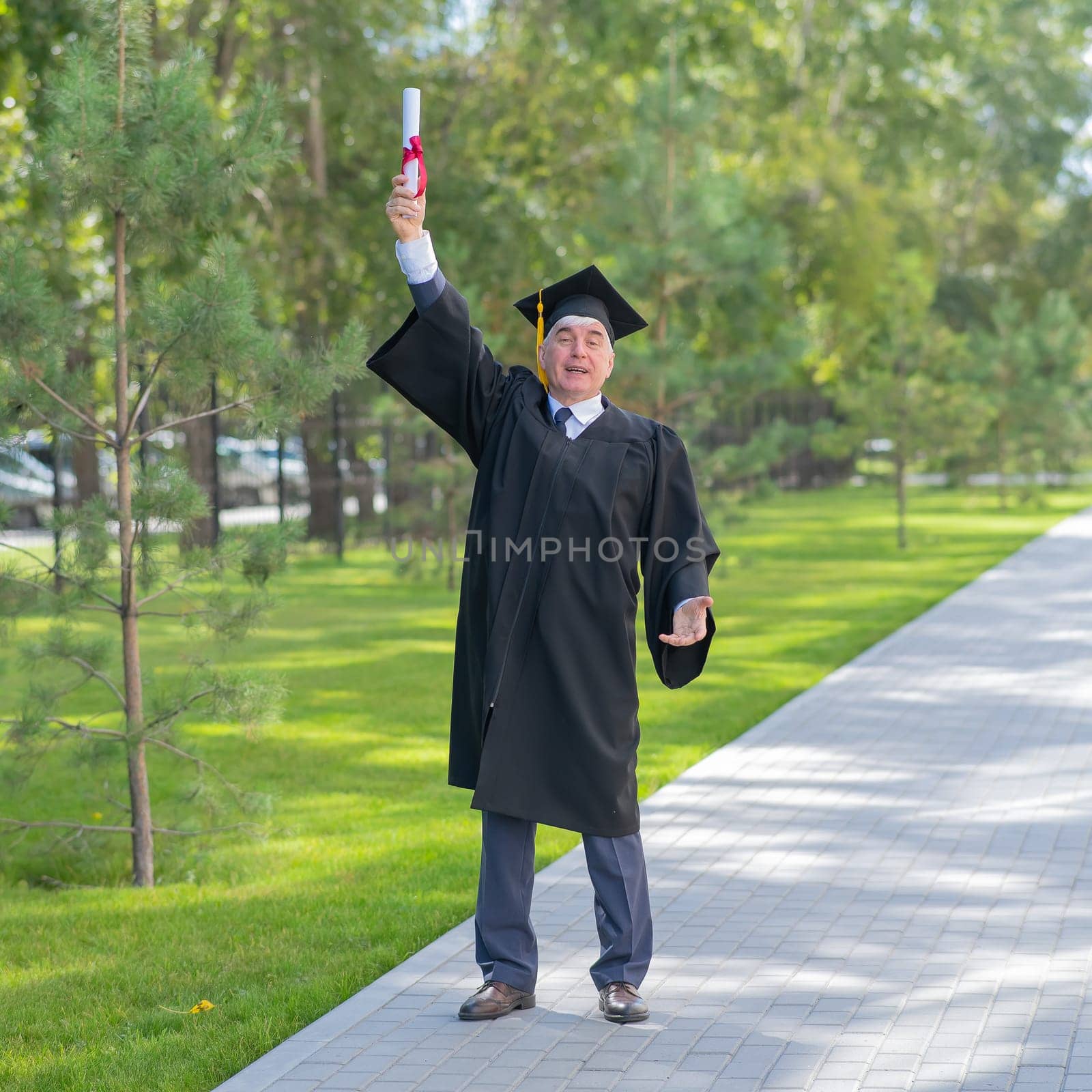 A serious old man in a graduate robe pulls his hand with a diploma up outdoors. by mrwed54