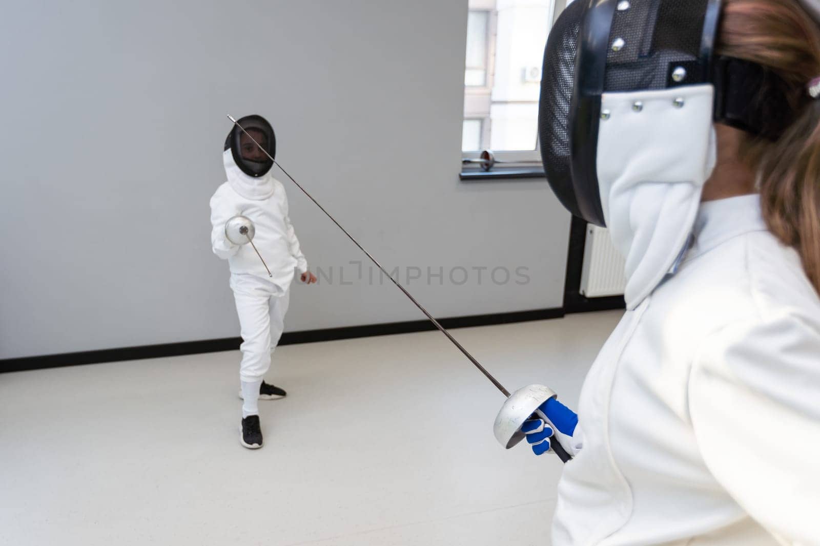 Children lunge on swords. A child in a class at a fencing school by Andelov13