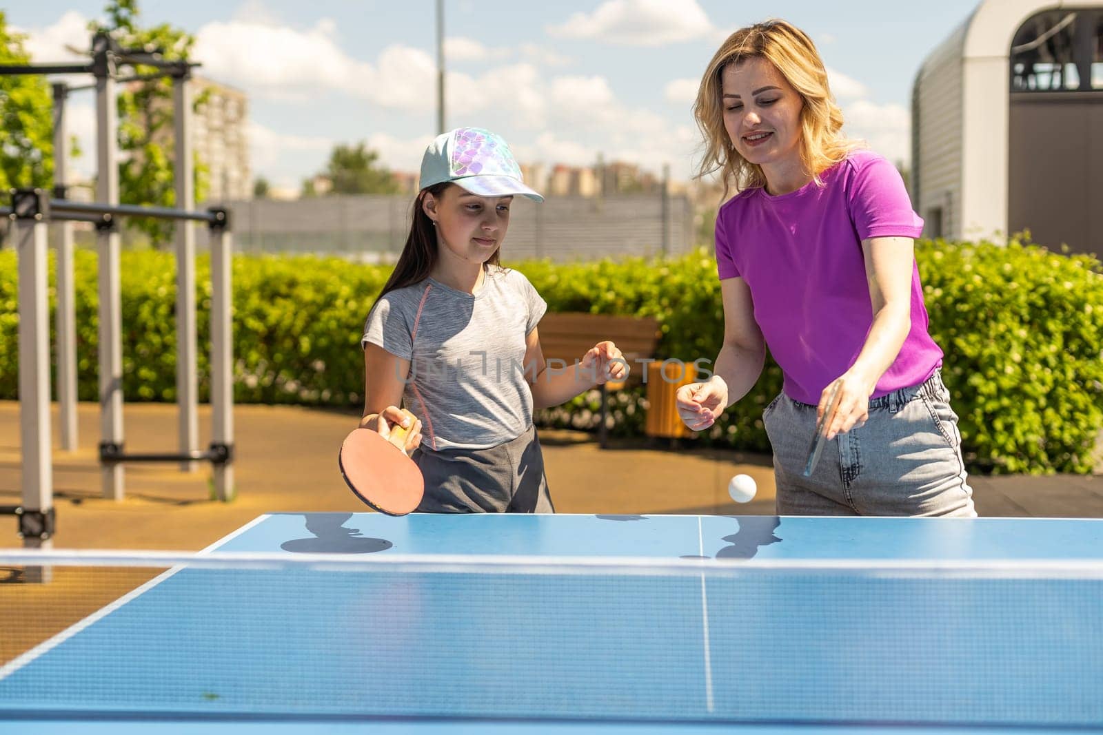 Young woman with her daughter playing ping pong in park by Andelov13