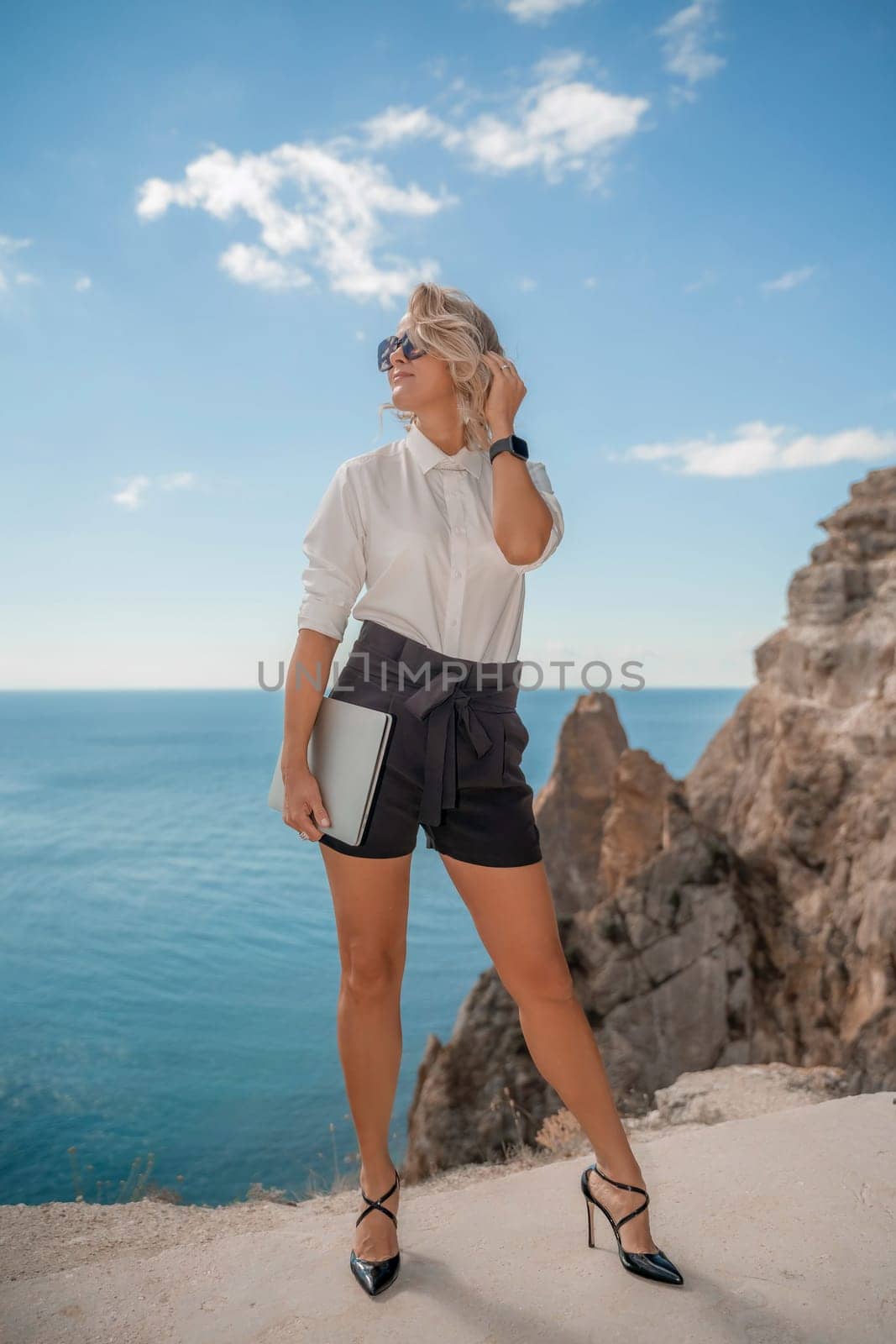 Freelance women sea working on a computer. Pretty middle aged woman with computer and phone outdoors with beautiful sea view. The concept of remote work