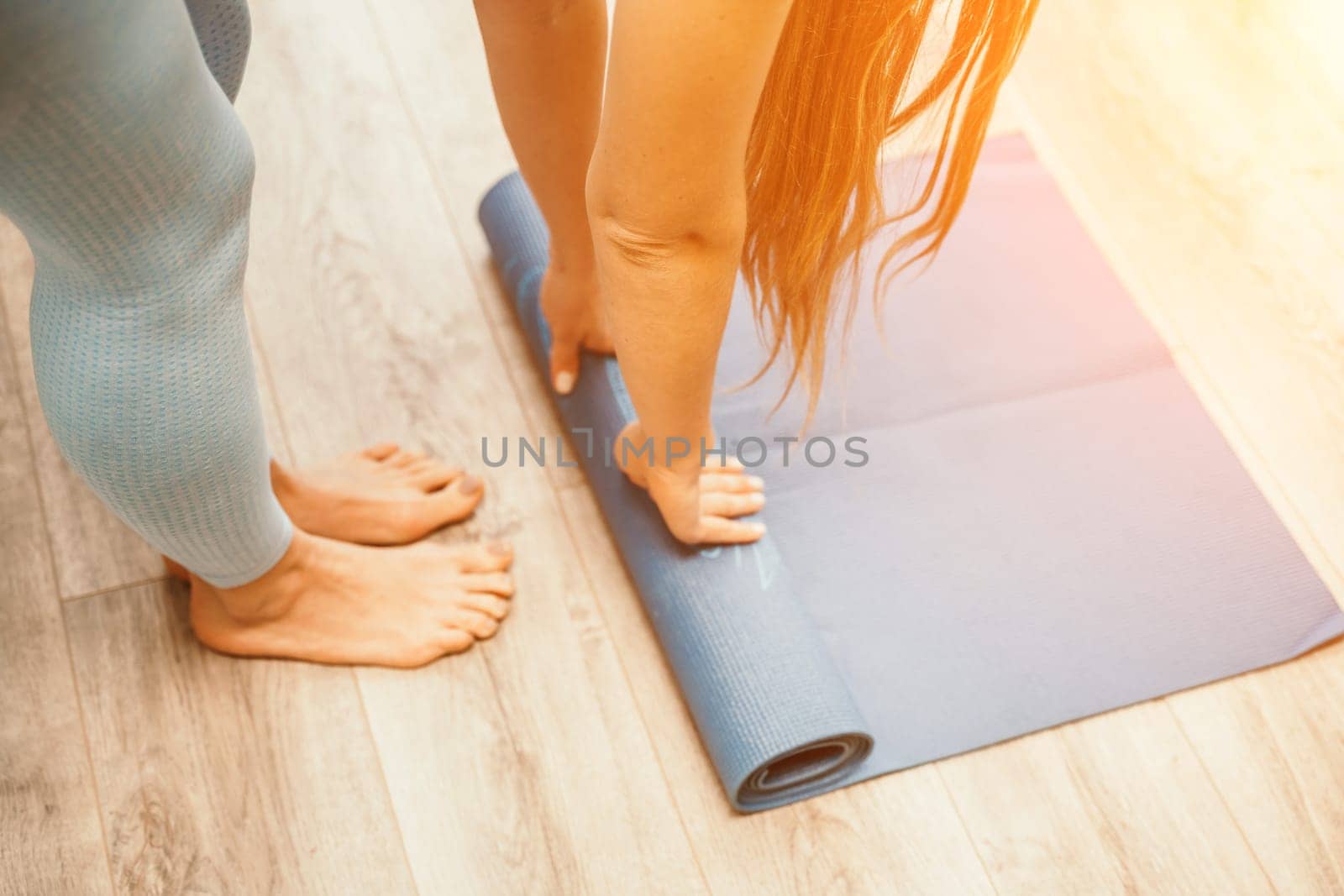 Woman hands rolled up yoga mat on gym floor in yoga fitness training room. Home workout woman close up hands rolling foam yoga gym mat. Woman barefoot home workout sportive healthy lifestyle concept.